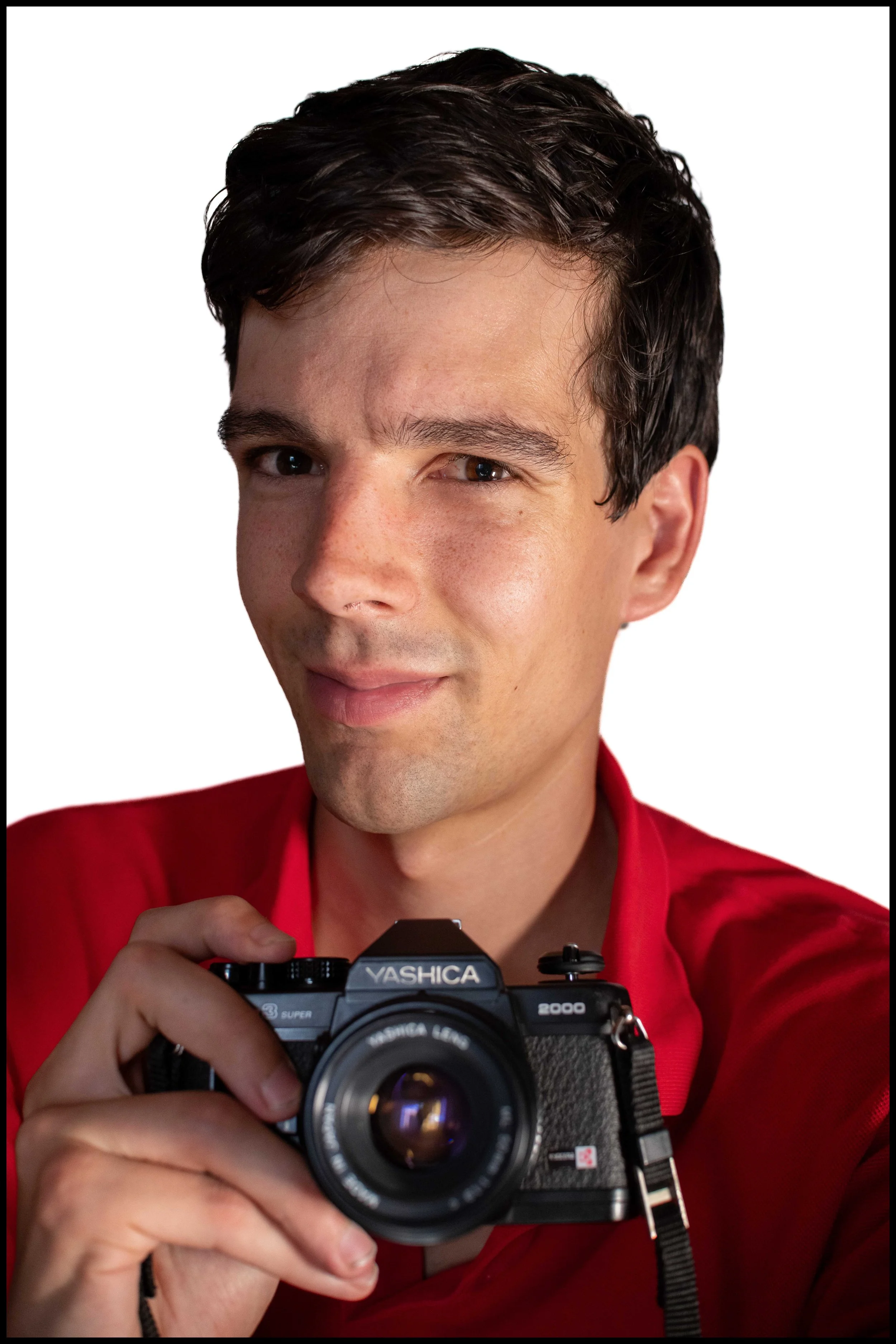 Un homme tient un appareil photo Yashica, se préparant à prendre une photo. Il porte une chemise rouge et a les cheveux bruns.