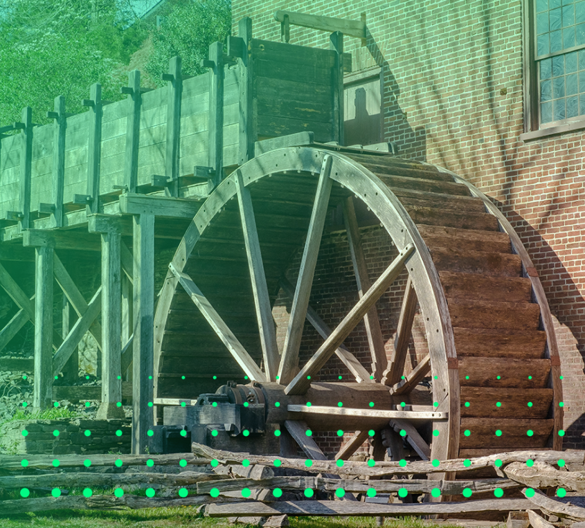 A large wooden water wheel attached to an old brick building with a wooden walkway above it.