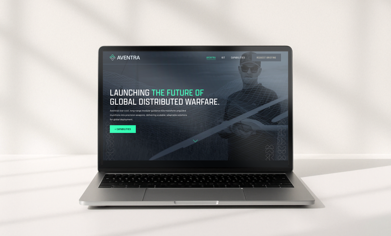 Open laptop displaying a website for AVENTRA, with a slogan about launching the future of global distributed warfare, positioned on a white surface and against a white wall.