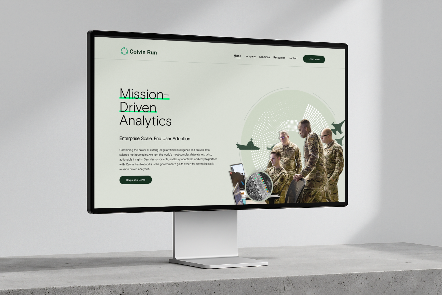 A large digital display monitor on a stand showing a website for 'Colvin Run' with a headline 'Mission-Driven Analytics' and an image of military personnel viewing a digital screen.