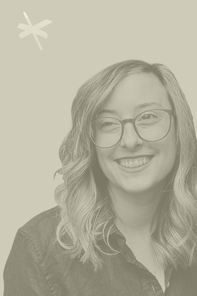 A woman with shoulder-length wavy blonde hair and glasses, smiling and looking slightly to her left, wearing a dark denim shirt.