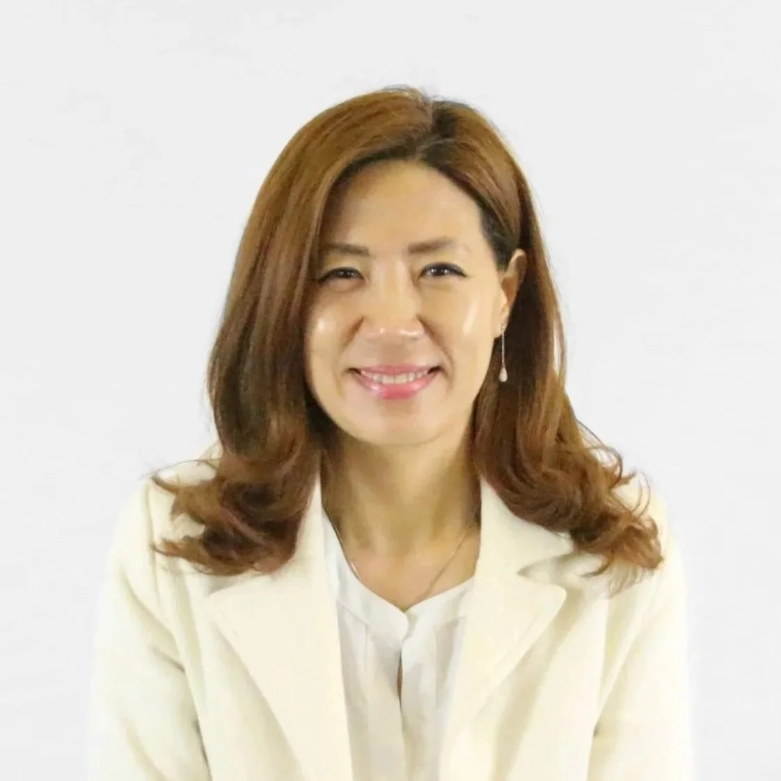 Portrait of an Asian woman with shoulder-length brown hair, smiling, wearing a cream blazer and white top, against a plain white background.