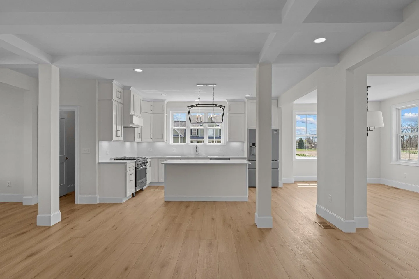 In this layout, the kitchen flows seamlessly into the surrounding living spaces, creating a home that feels both open and defined. Structural columns and ceiling details subtly frame each area while still allowing natural light and movement to carry 