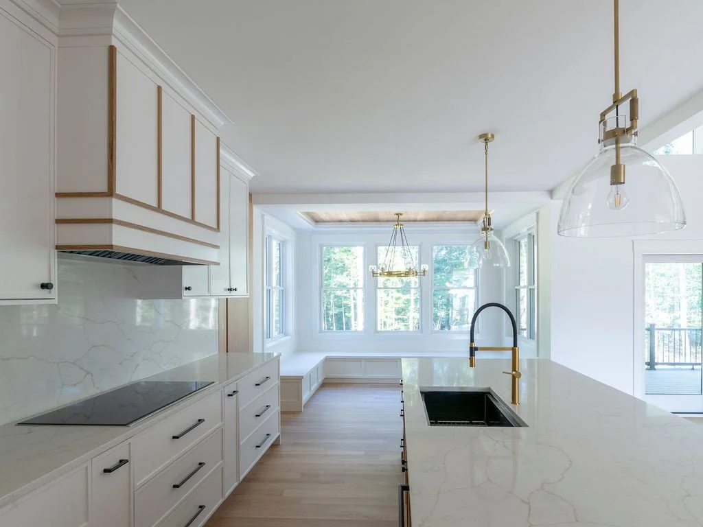 A kitchen designed to feel open, functional, and full of light. Clean cabinetry, warm wood accents, and subtle brass details create a balanced, refined palette, while the oversized island anchors the space for both everyday use and gathering. Surroun