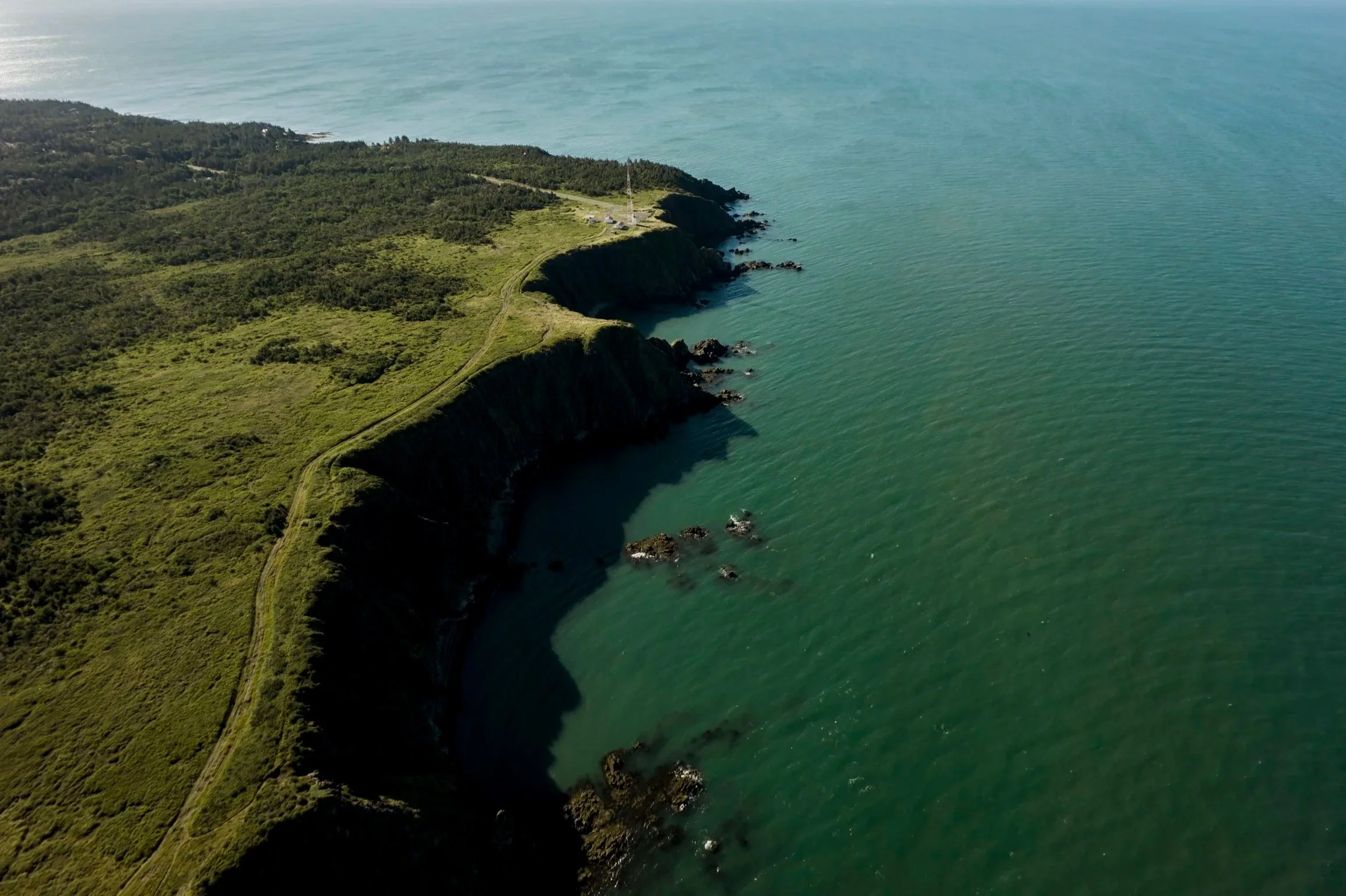 Aerial view of green coastal cliffs with rugged rocks in the ocean.