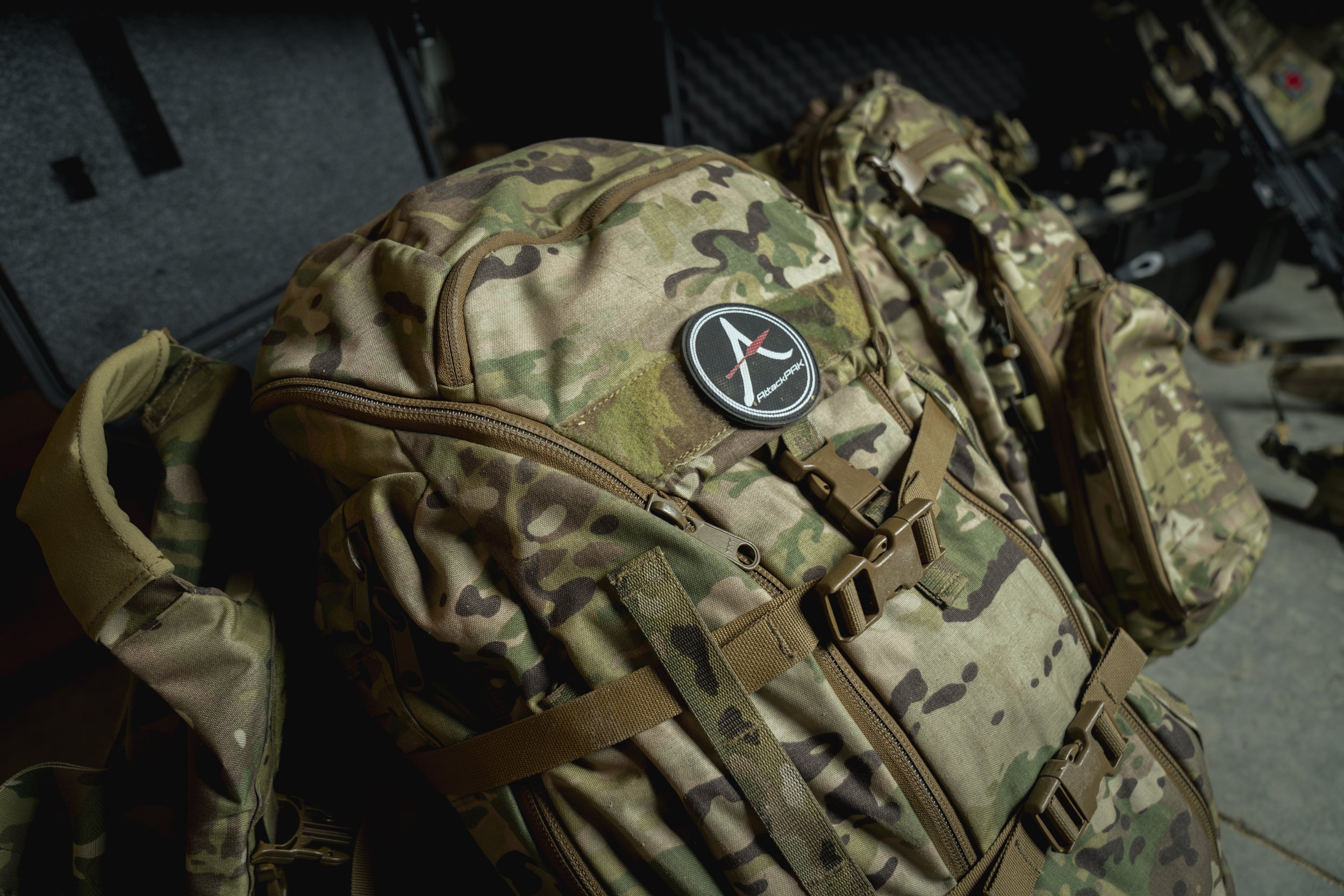 Multiple camouflage military backpacks with front zippers, straps, and patches, displayed on a table.