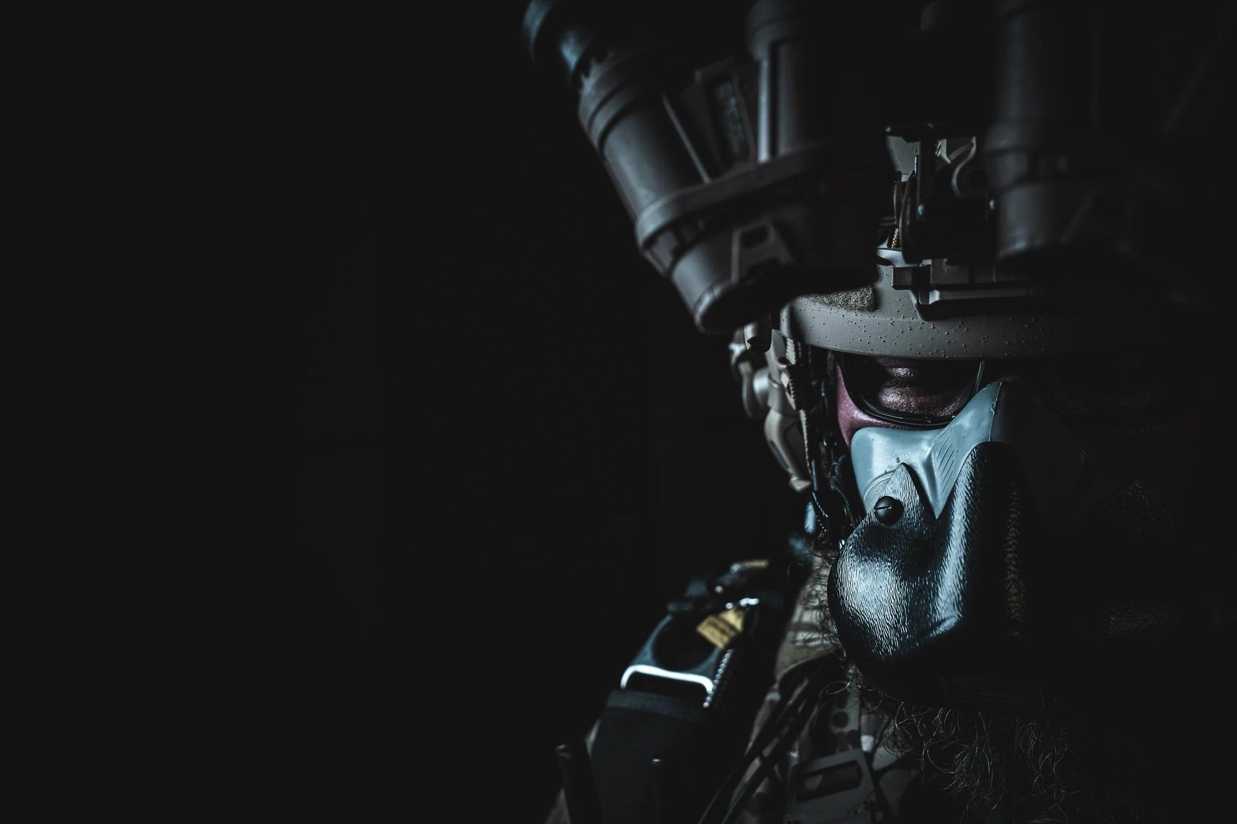 Close-up of a soldier wearing tactical gear, including a face mask and helmet, with dark background.