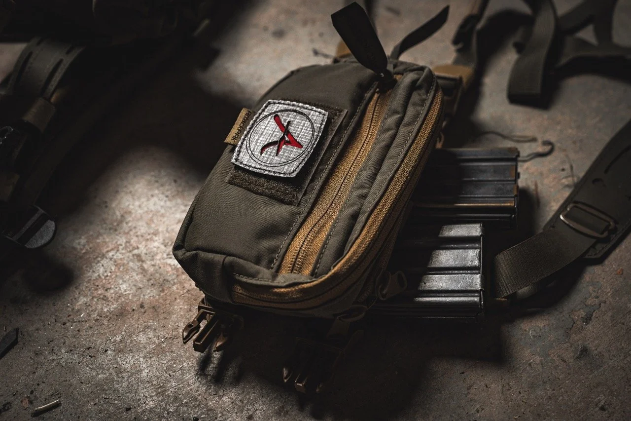 A green tactical pouch with a patch, lying on the ground next to magazines and other gear.