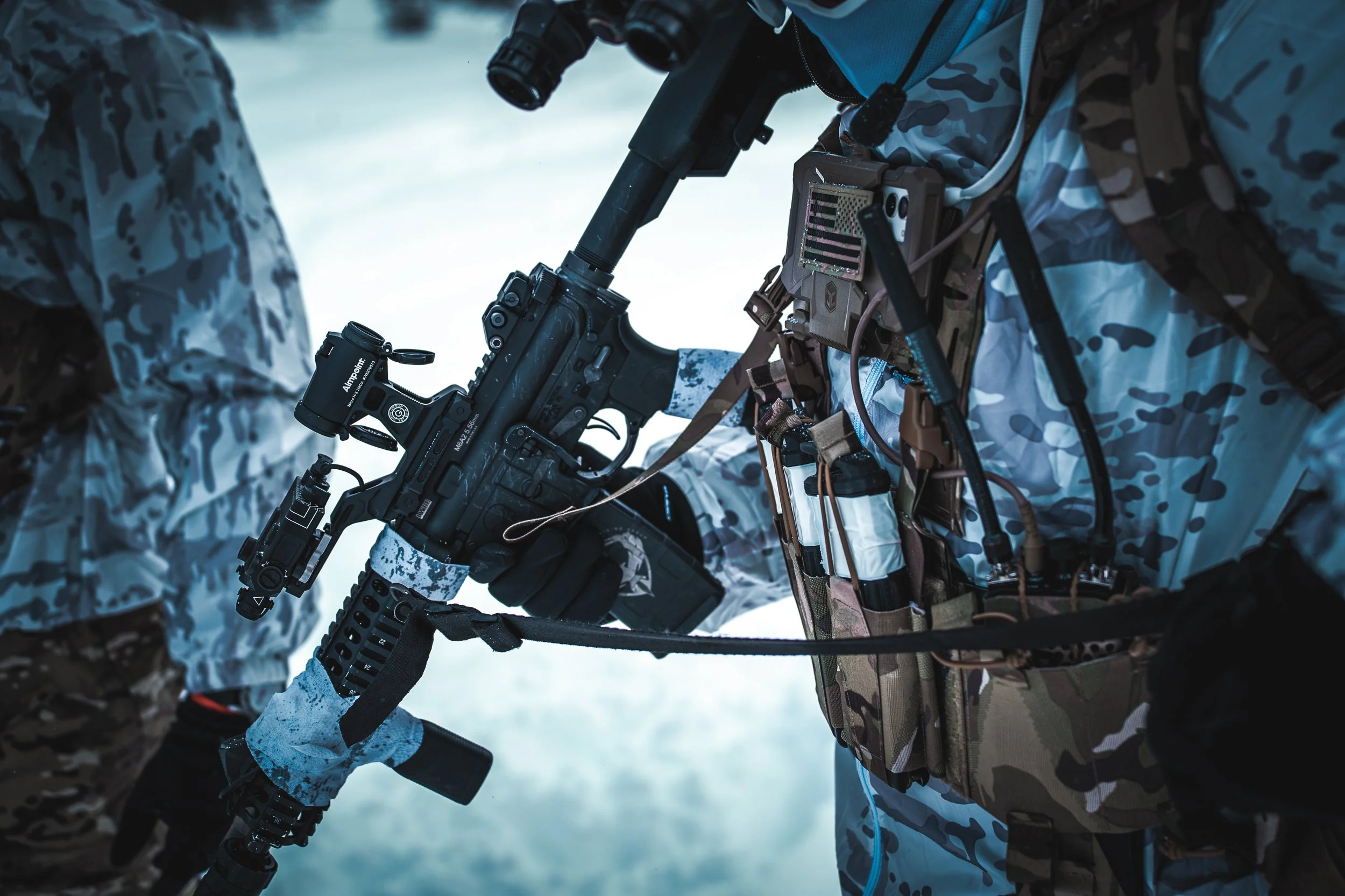 Close-up of a soldier in camouflage gear holding a rifle with a scope in a snowy environment.