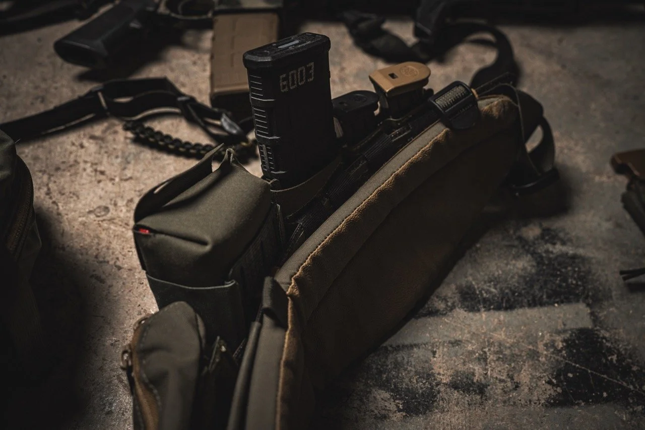 Tactical belt with attached pouches and a holstered firearm, laid on a rough surface.