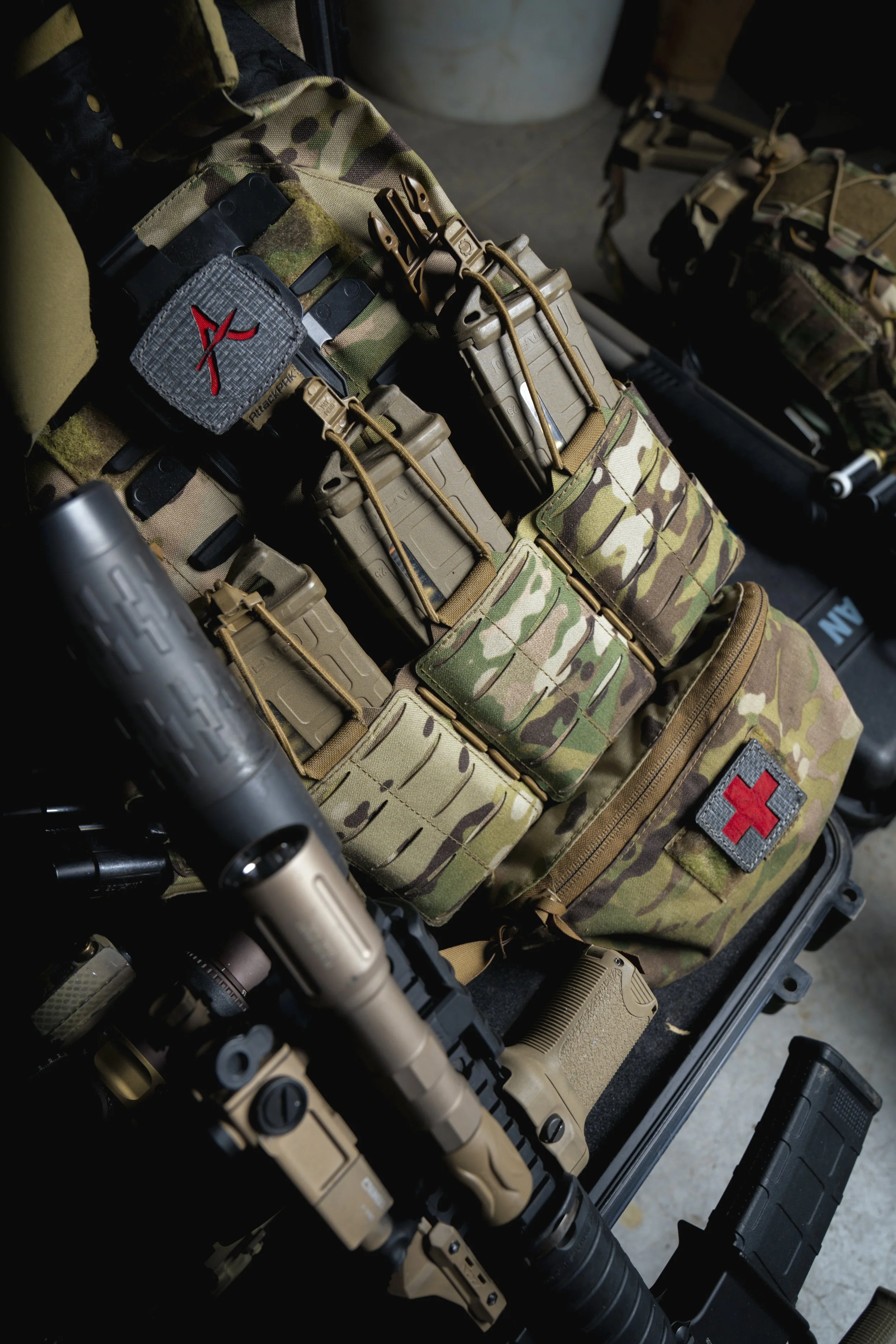 Military or tactical gear laid out, including camouflage pouches, medical patch with a red cross, and a tactical flashlight.