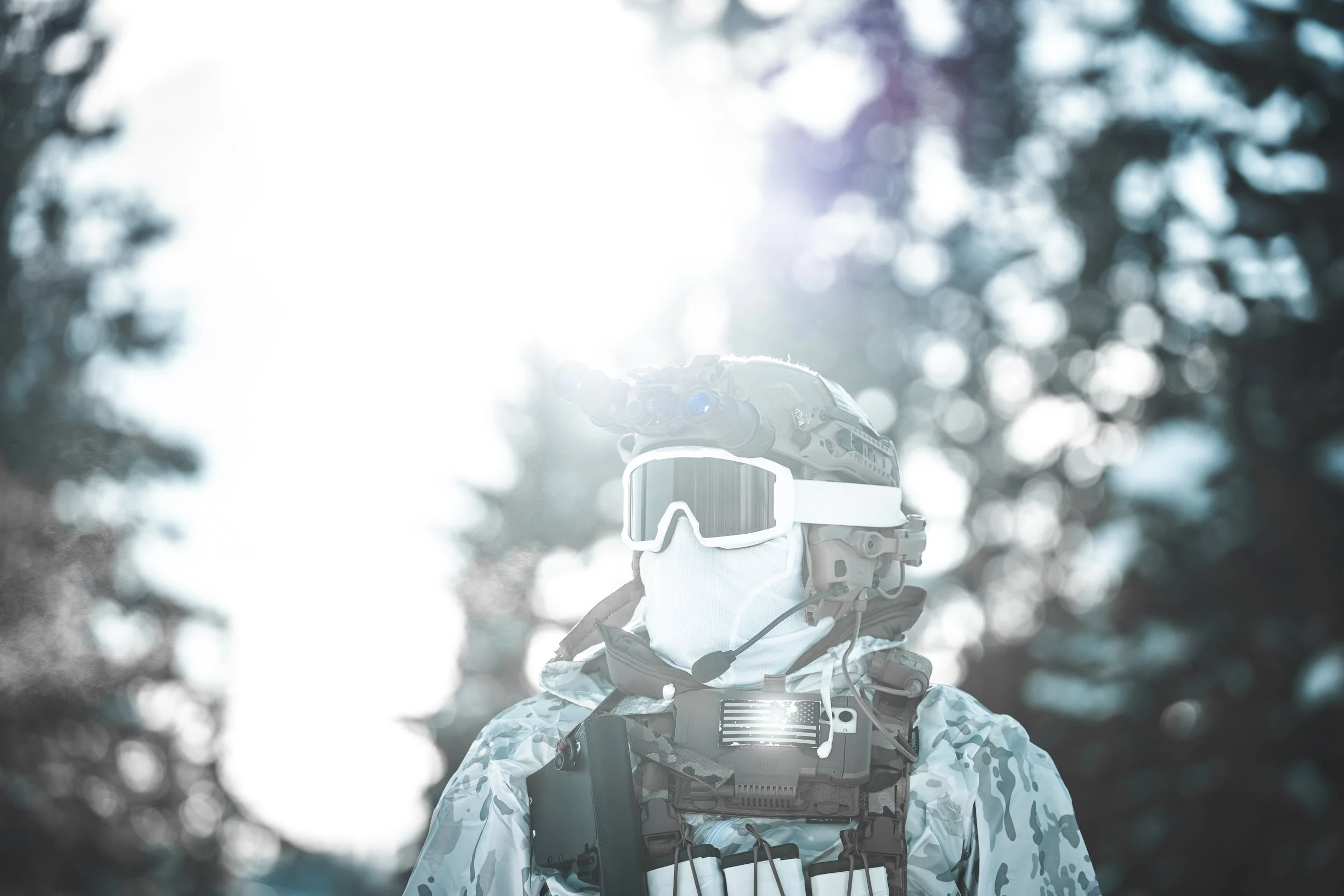A soldier wearing military gear, goggles, a mask, and camouflage clothing with a dark background and bright sunlight.