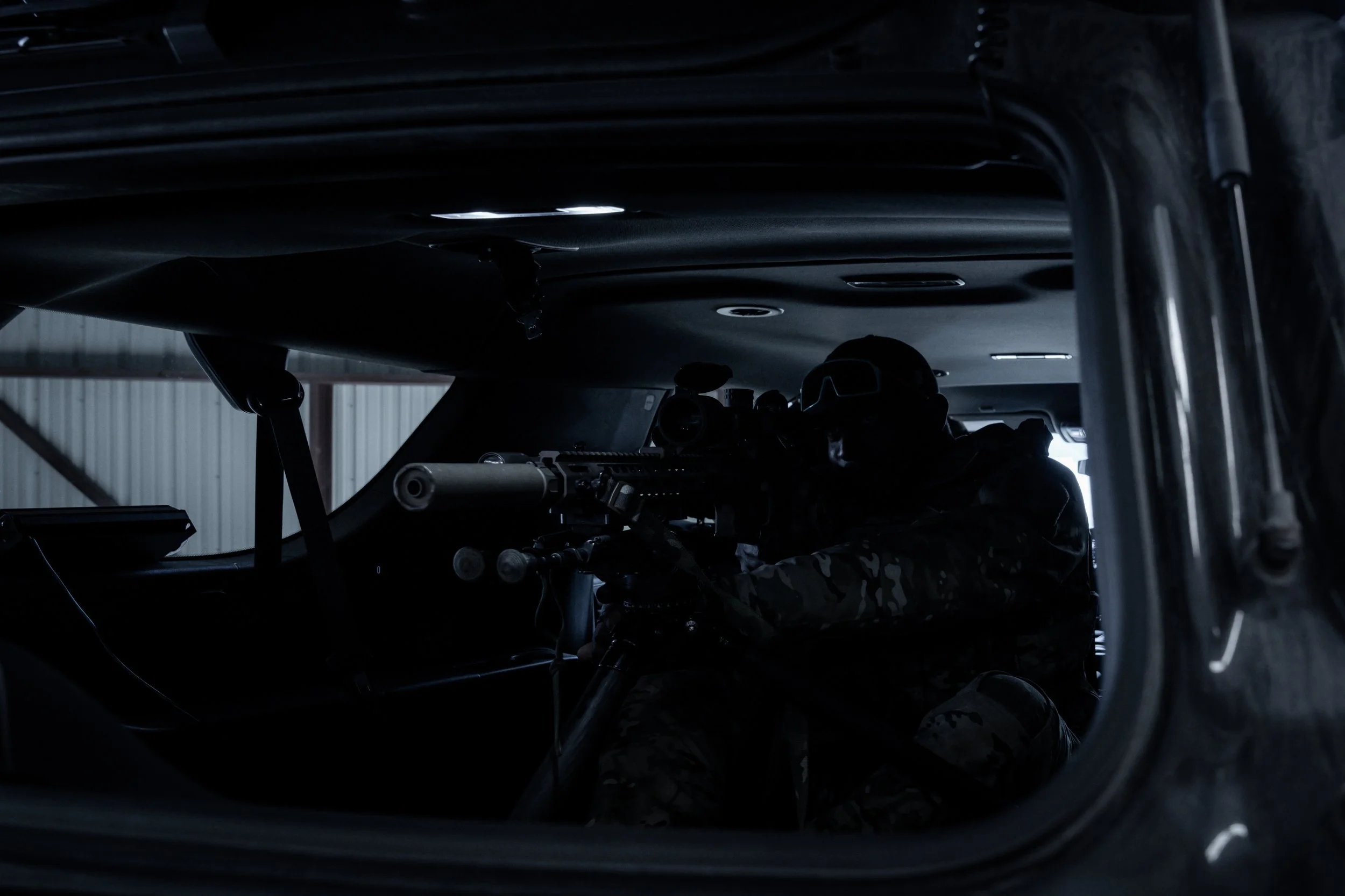 Silhouette of a soldier aiming a rifle inside a dark vehicle.