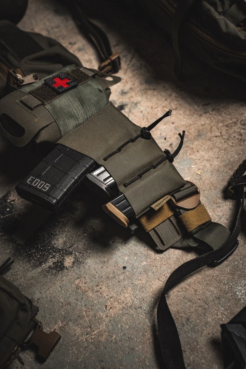 A tactical firearm with attached accessories and pouches lying on a concrete floor, surrounded by other gear.