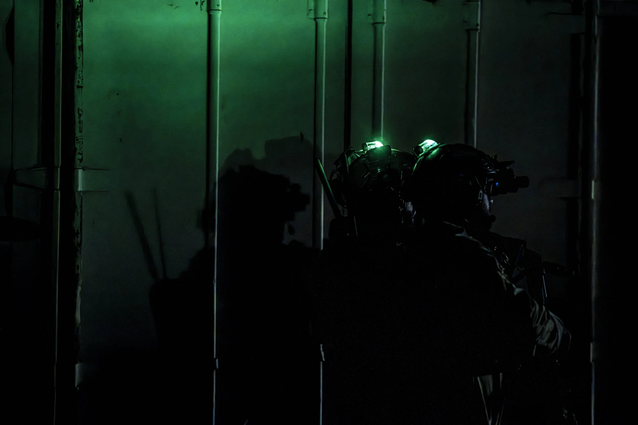 Silhouette of a soldier wearing night vision goggles in a dark environment with a greenish glow.