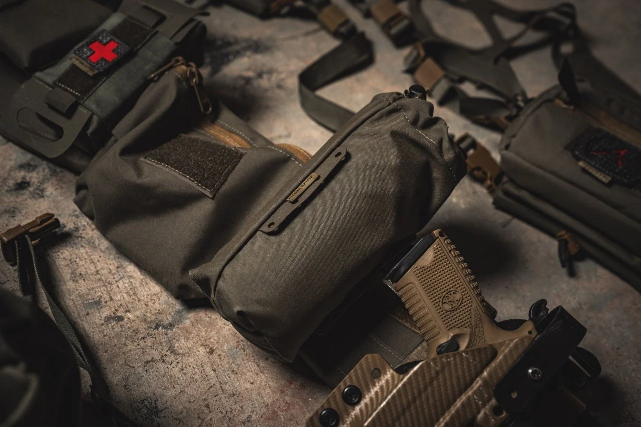 A collection of tactical gear, including a gray duffel bag, a holstered pistol, and pouches, spread out on a rough surface.