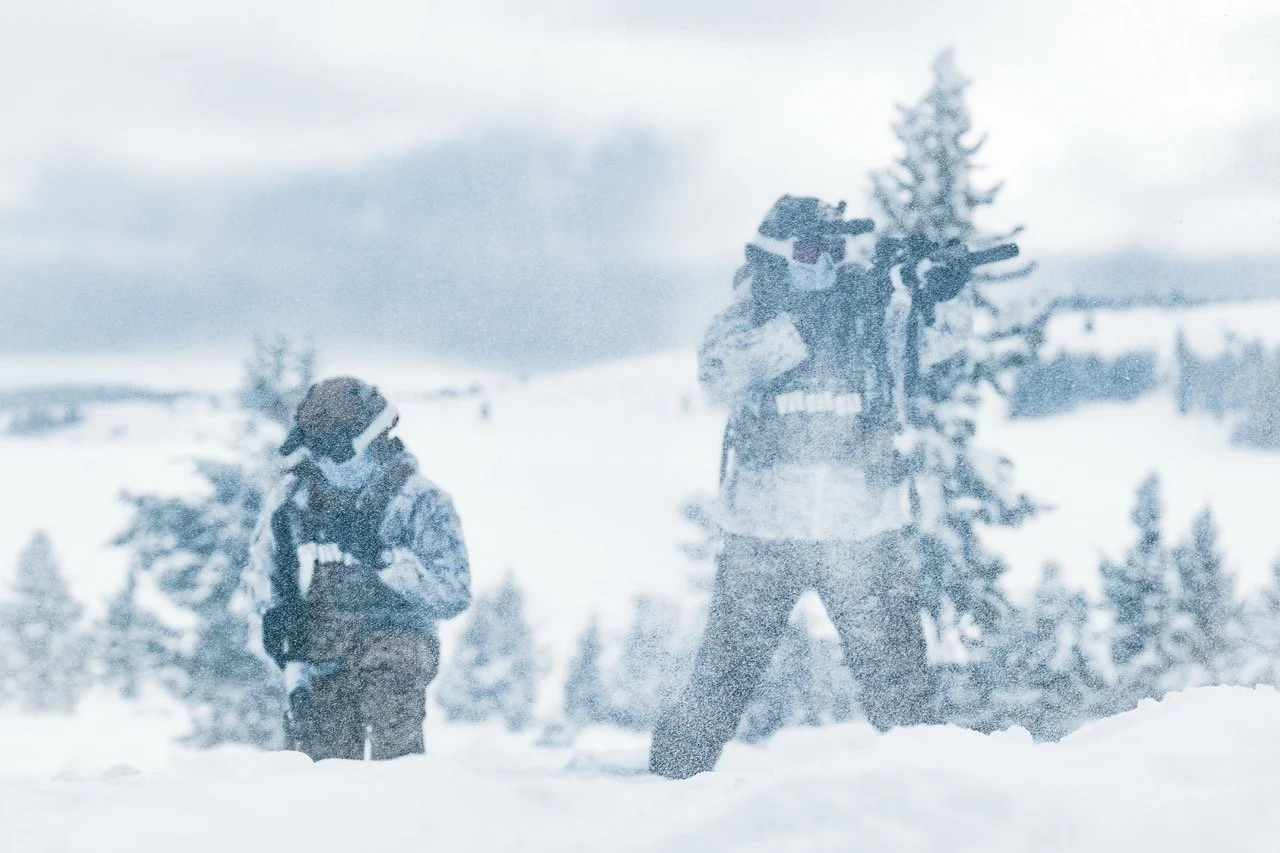 Two children dressed in winter clothing playing in a snowy landscape with trees in the background.