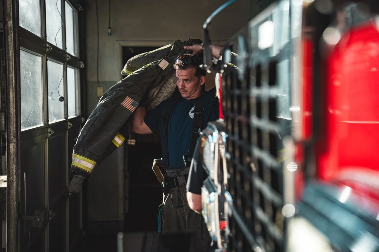 Firefighter with a patched uniform loading gear into a fire truck.