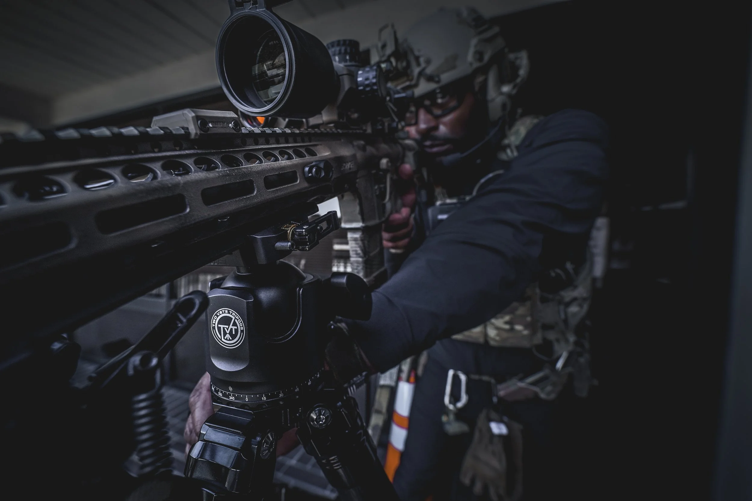A soldier in tactical gear aiming a sniper rifle through a scope.
