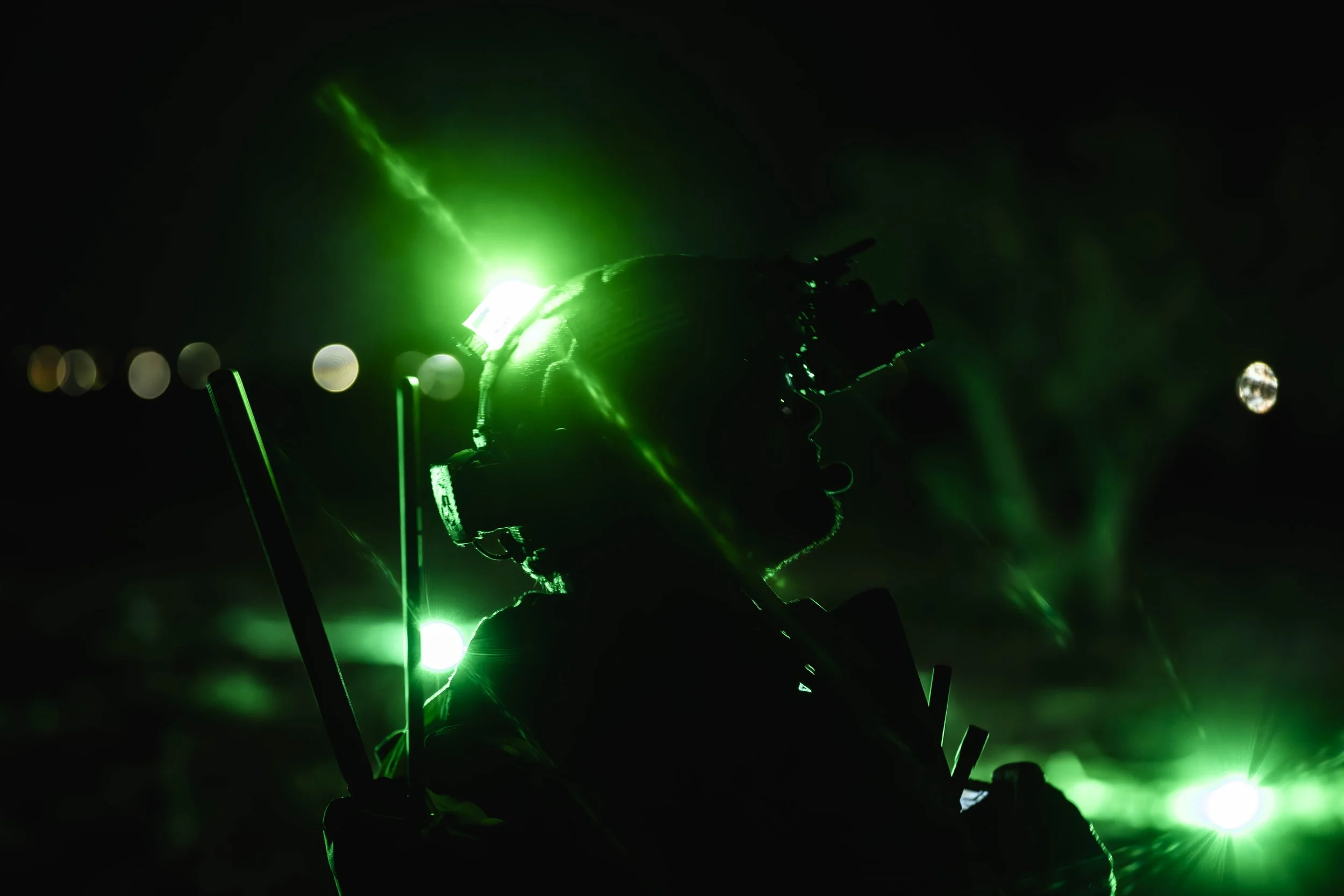 Silhouette of a scuba diver with a helmet and gear illuminated by green lights against a dark background.