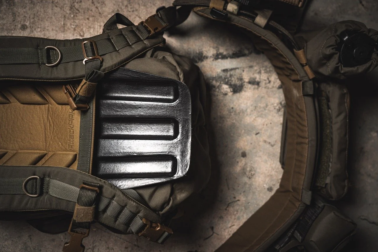 A tactical backpack with gear, including a black hard plastic container and rolled-up pouches, lying on a concrete surface.