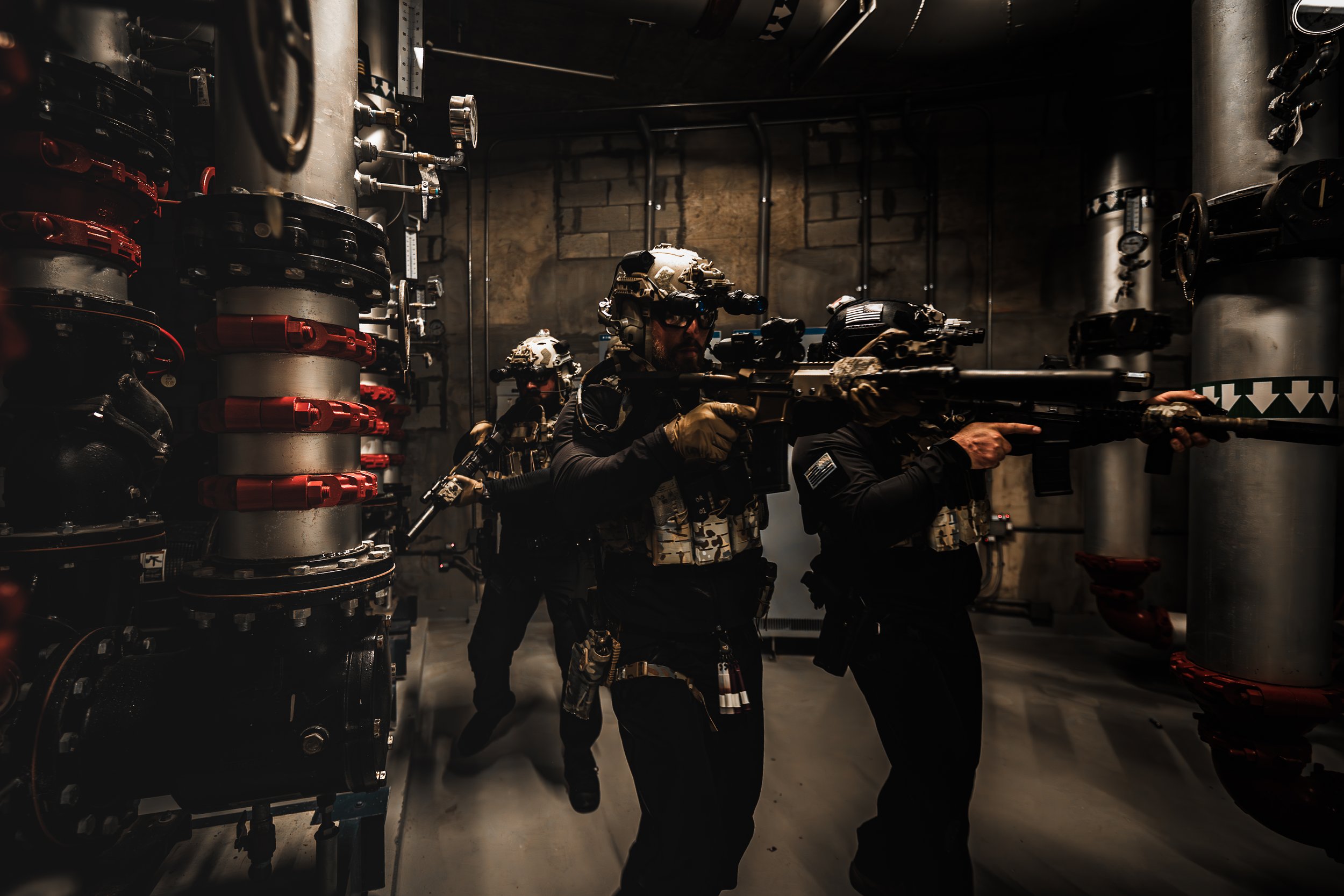 Military personnel in tactical gear aiming rifles in an industrial setting.