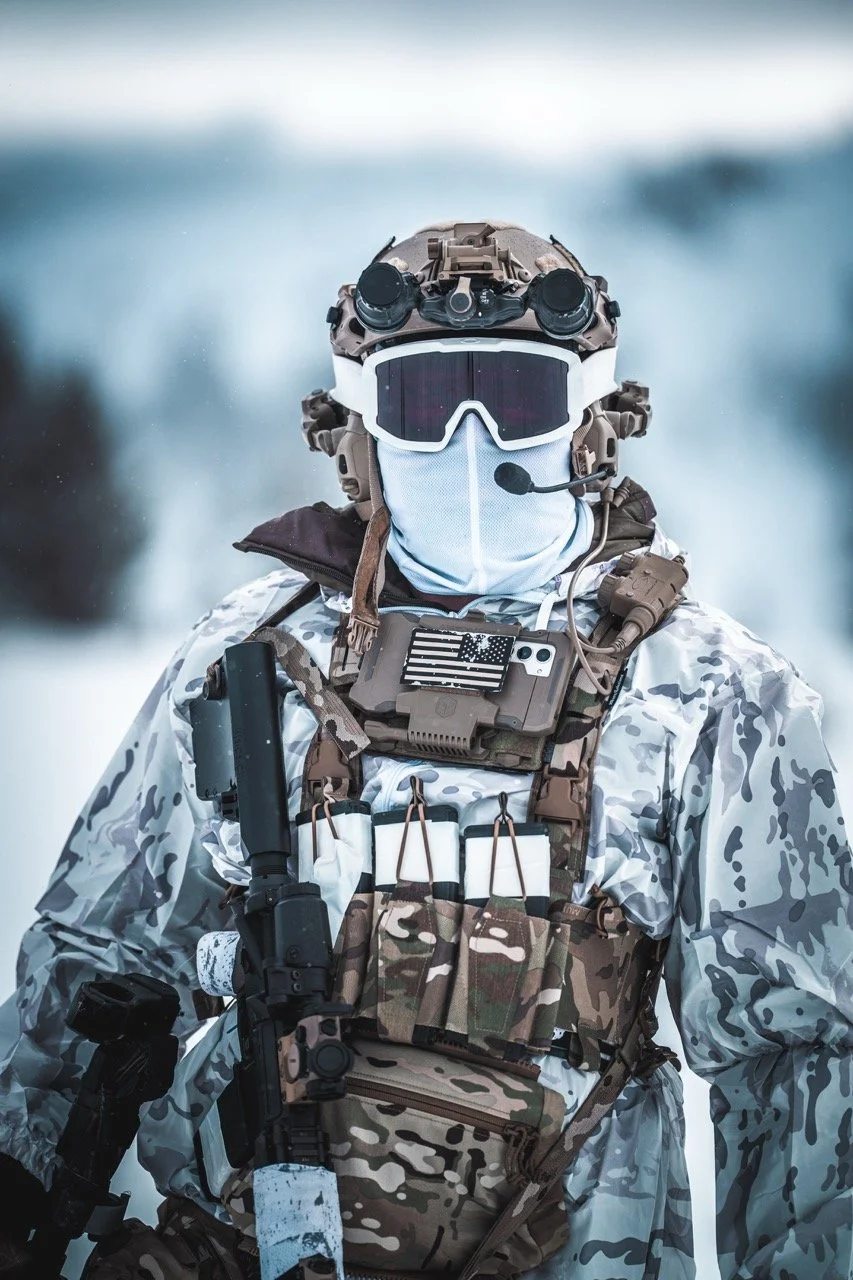 Military soldier in camouflage uniform equipped with tactical gear, helmet with night vision goggles, mask, and holding a rifle in a snowy environment.
