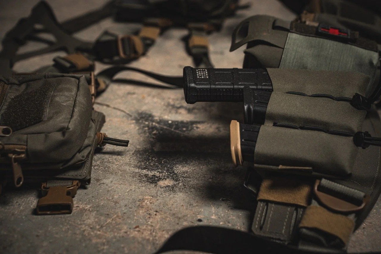 Military tactical gear including a holstered pistol, pouches, and straps laid out on a rough surface.