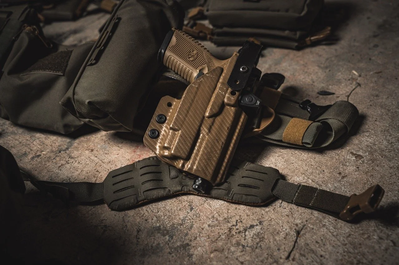 A tactical firearm in a holster, along with military gear, resting on a rough surface.