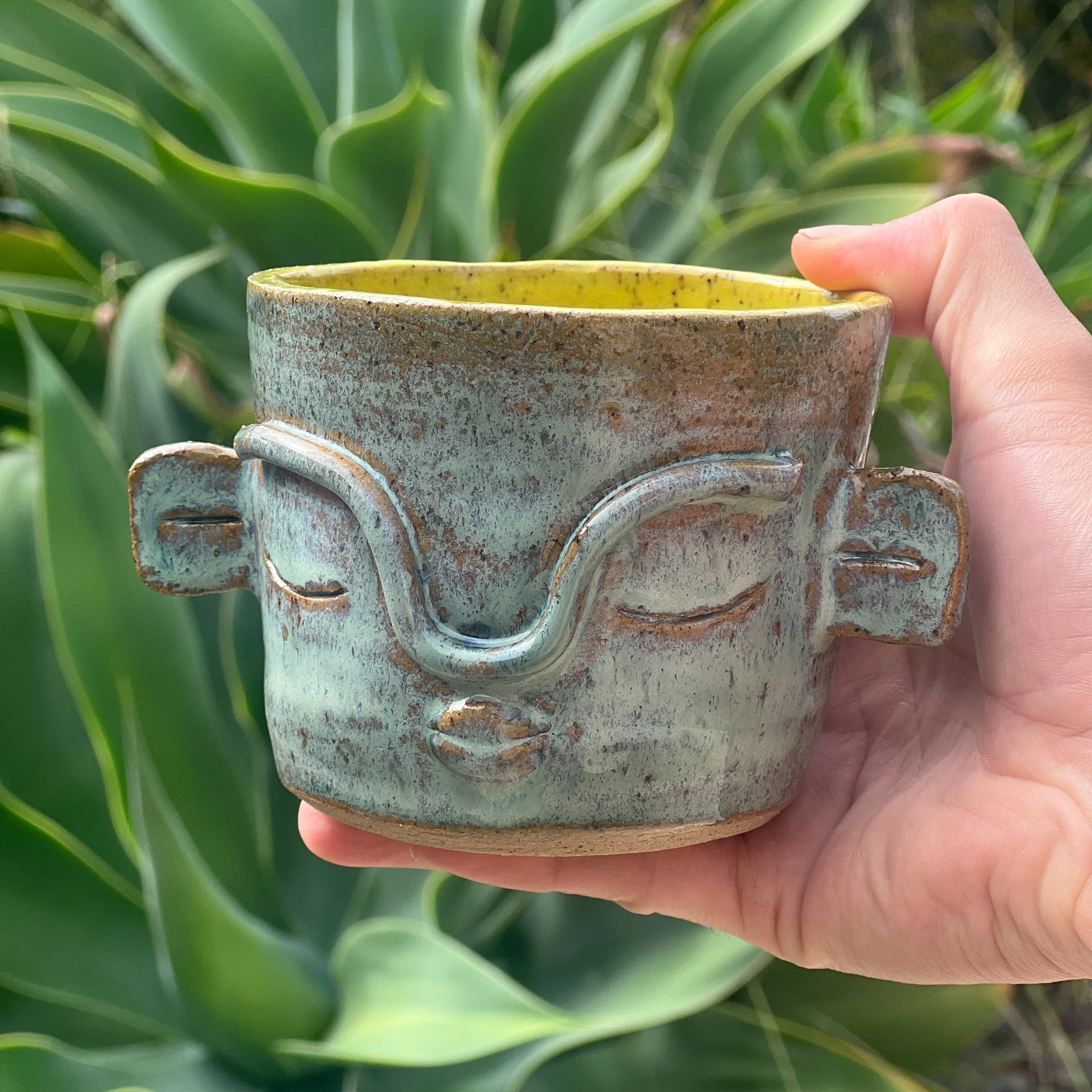Ceramic cup with face on it and yellow glaze inside
