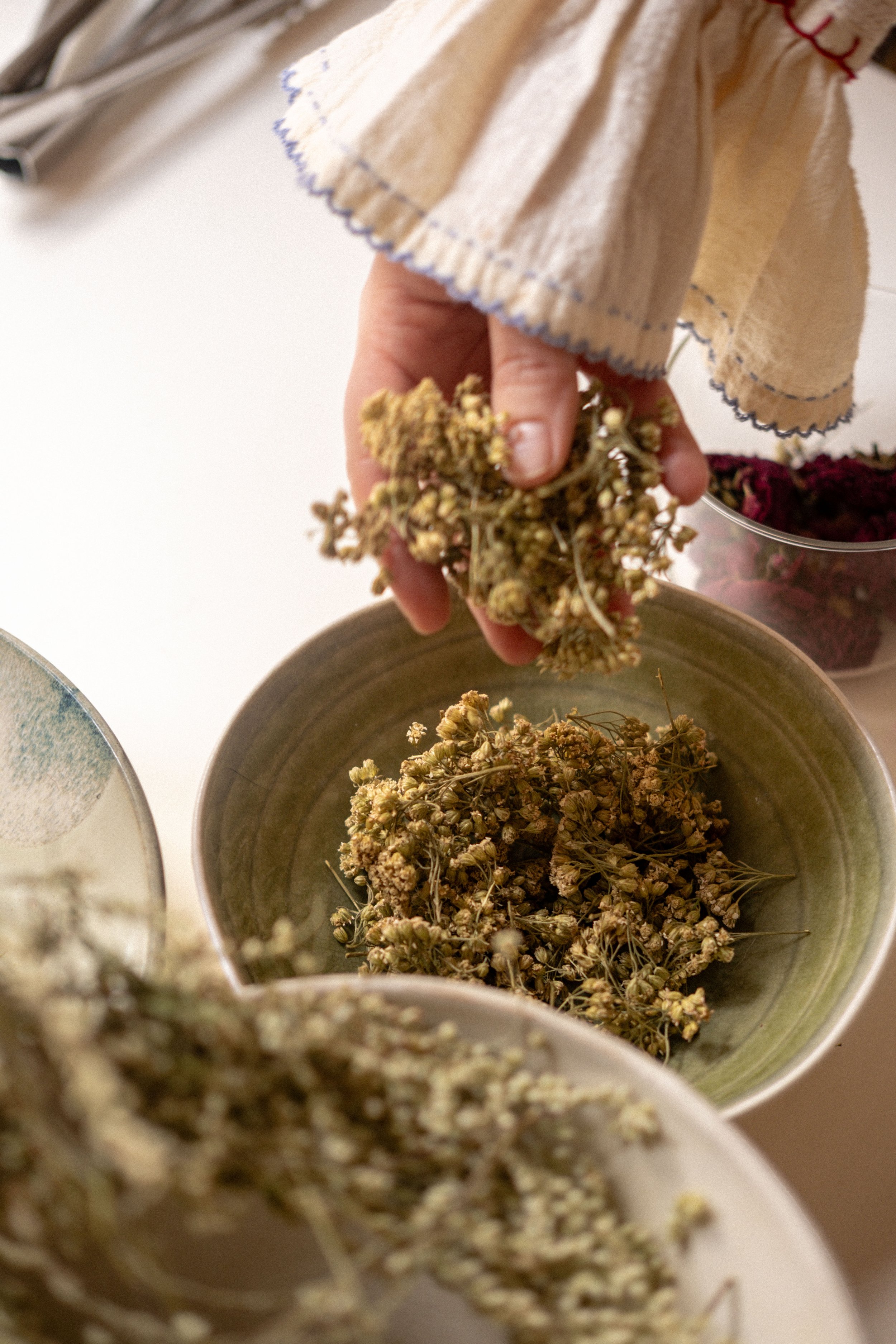 Une personne récoltant des fleurs séchées dans un bol, avec d'autres contenants de fleurs en arrière-plan.