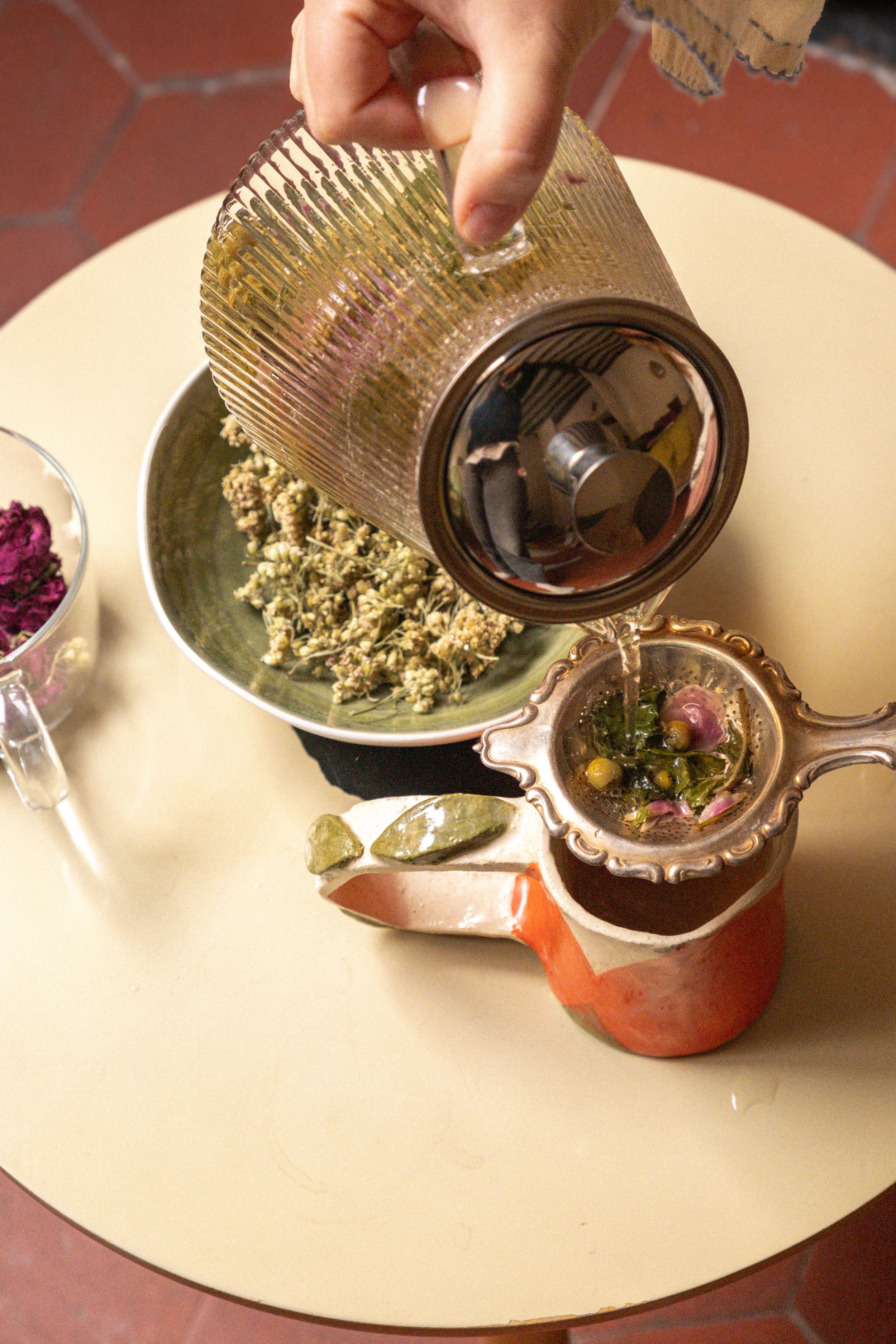 Une main verse une boisson dans une tasse décorative contenant des fleurs.