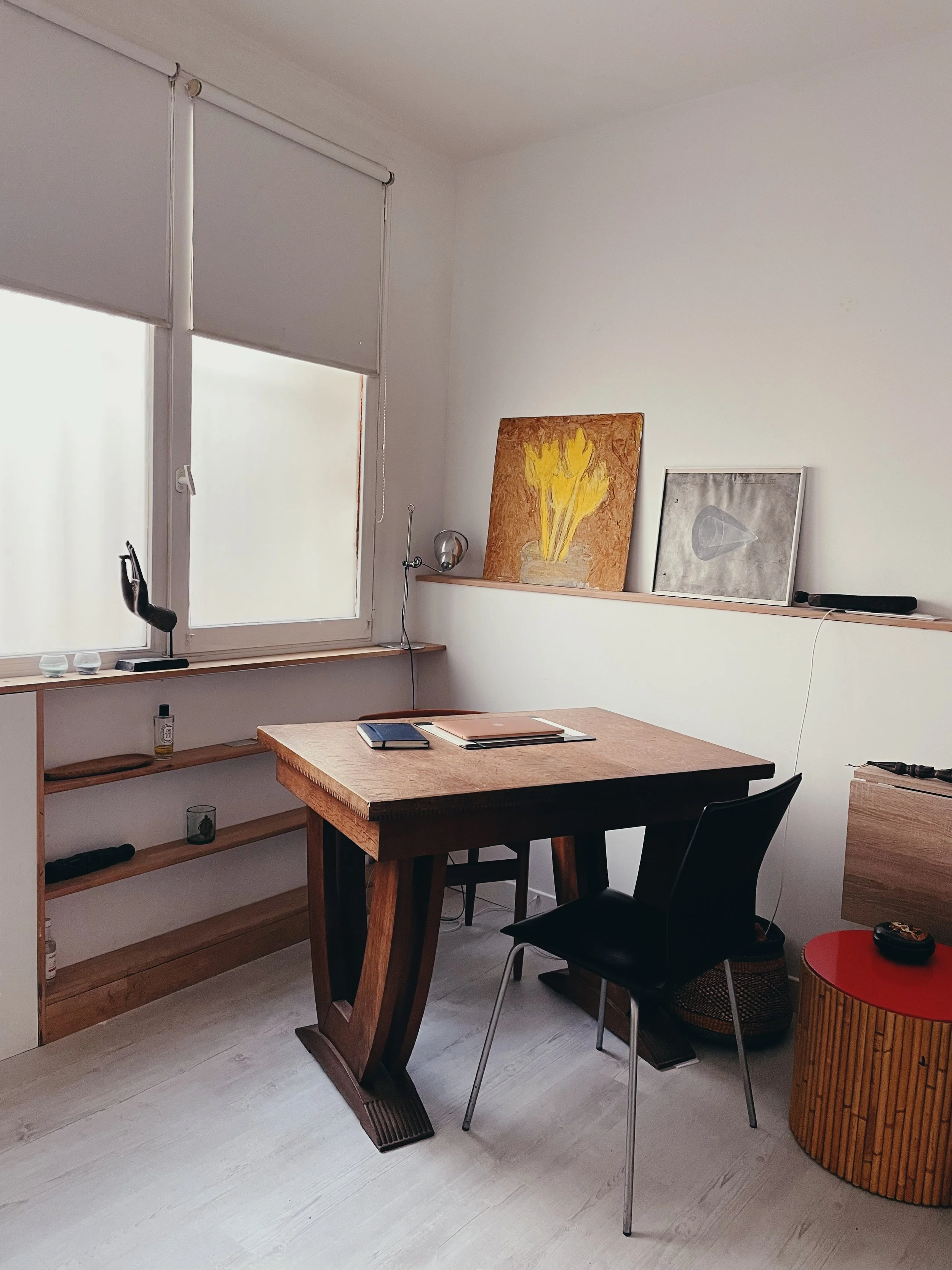 Ceci est un bureau minimaliste avec une fenêtre, un bureau en bois, deux chaises, et des œuvres d'art accroché au mur.