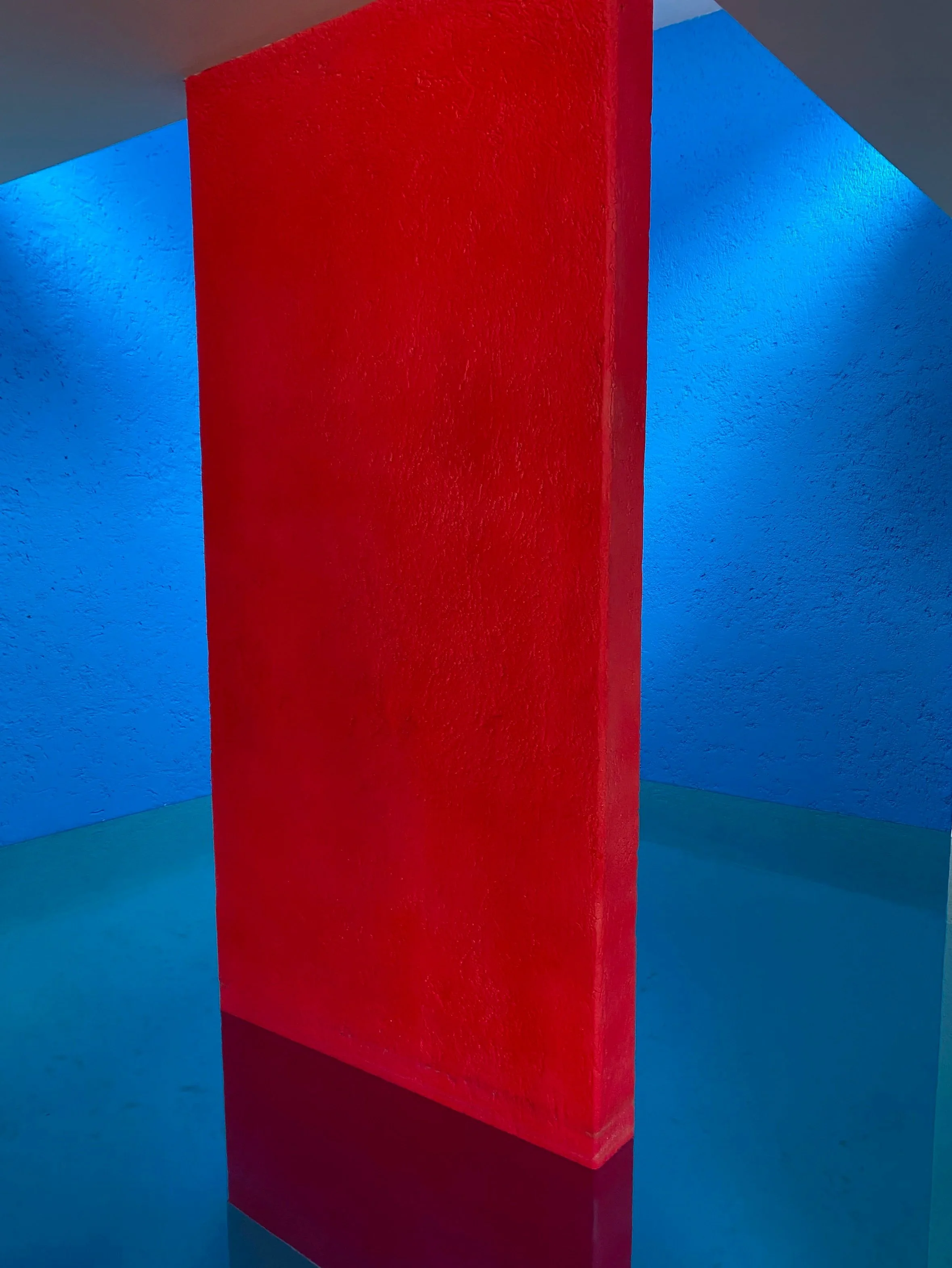 Interior of a colorful room with textured blue walls, a red freestanding wall in the center, and blue lighting accents.