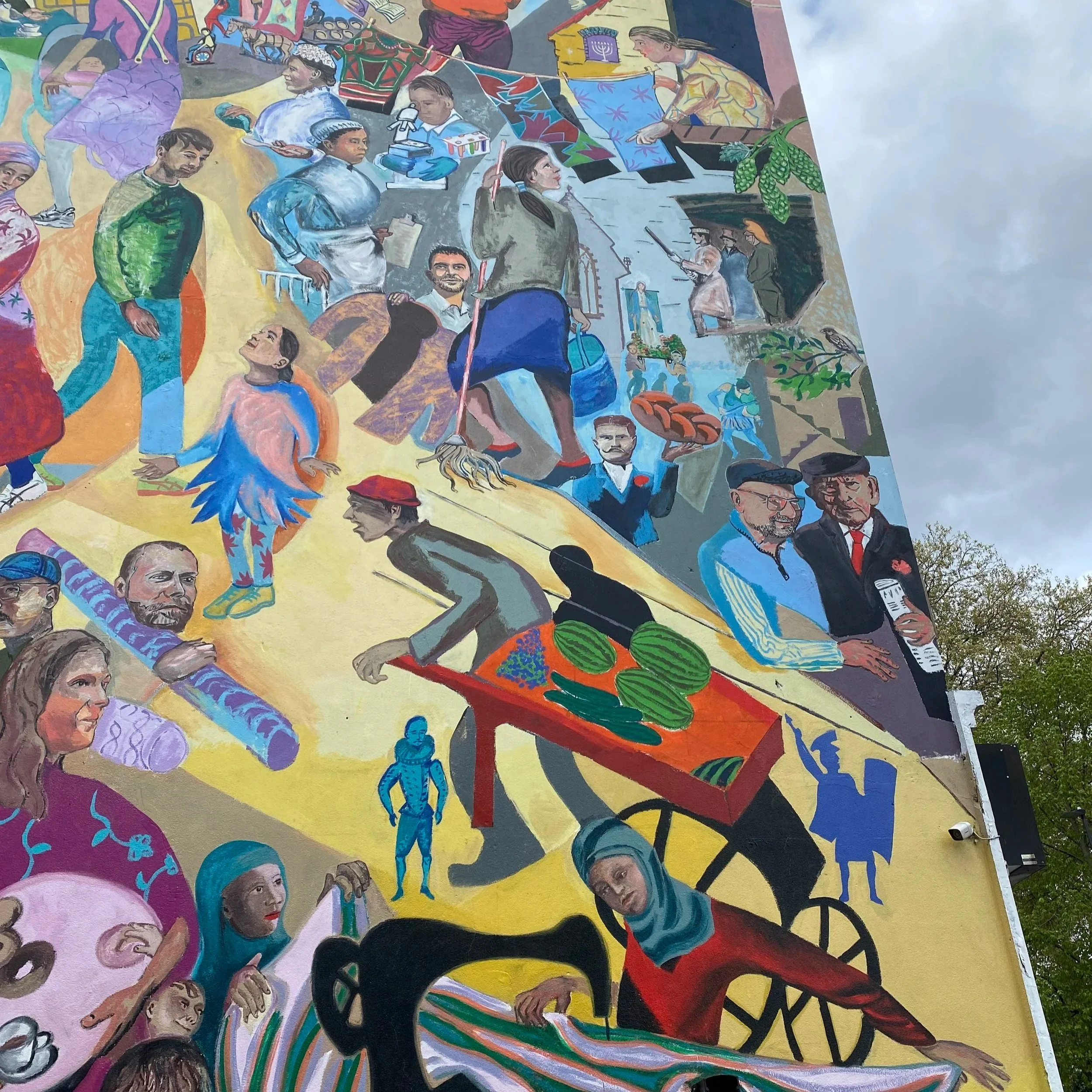 Colorful mural depicting diverse people engaging in various activities, including conversations, performing, selling, and interacting in a lively community scene.