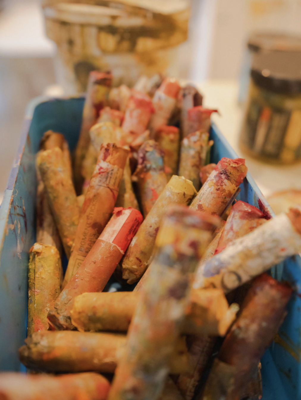 A blue container filled with used, colorful oil pastels with caked-on paint.