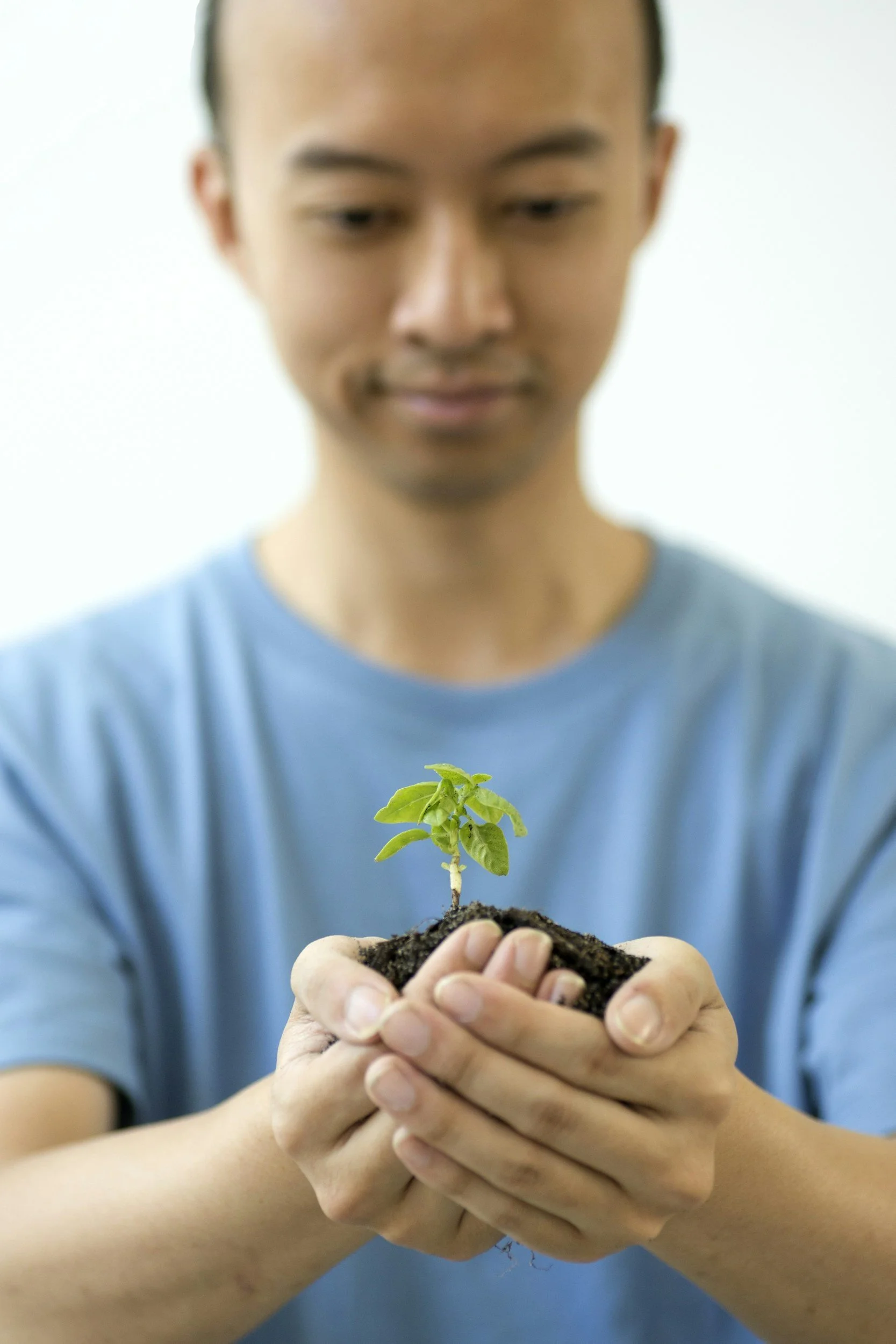 Man holding soil with a small green plant in his hands, wearing a blue t-shirt.