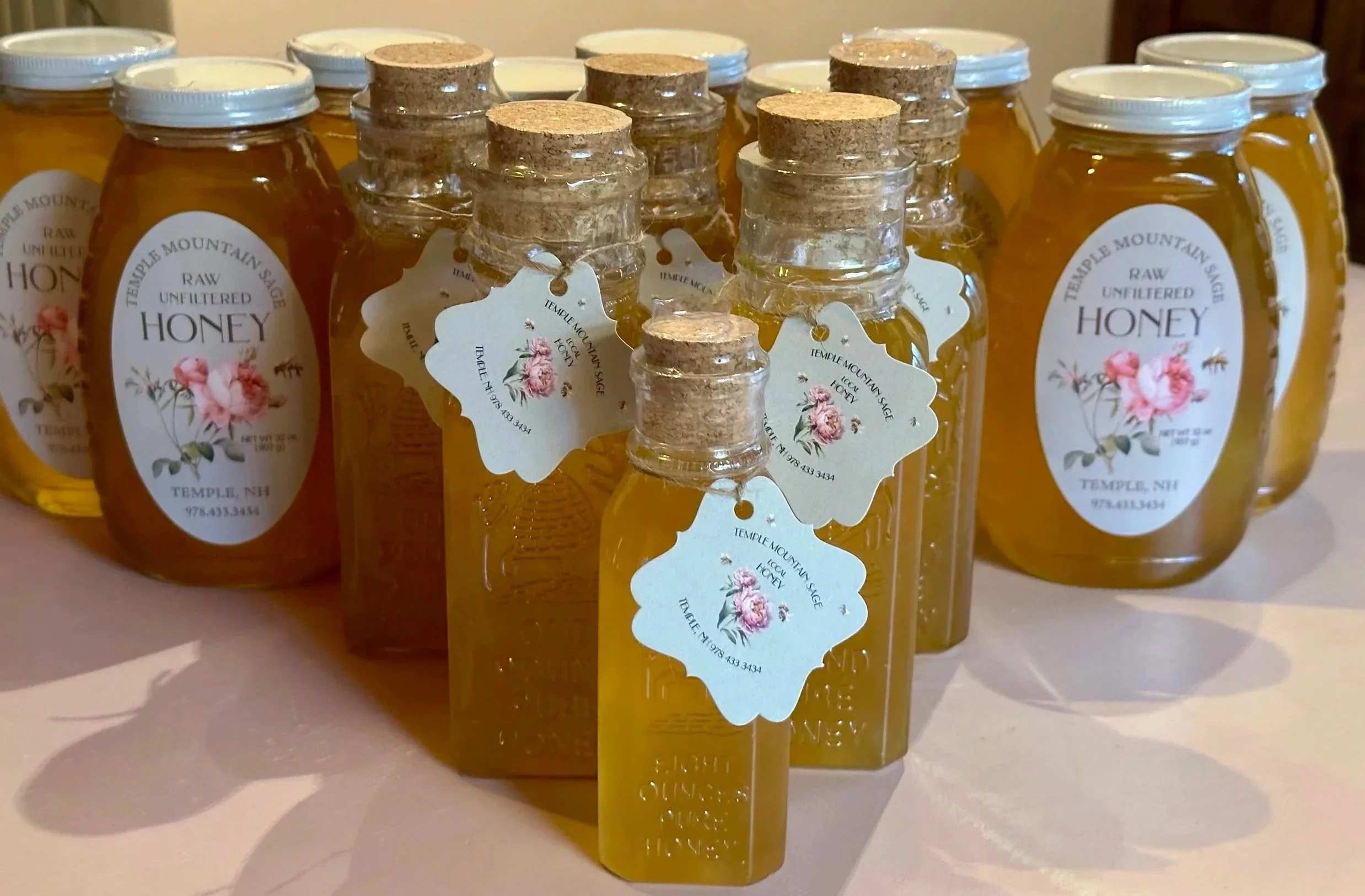 Several jars of raw, unfiltered honey with white caps and labels, some with attached tags, arranged on a surface.