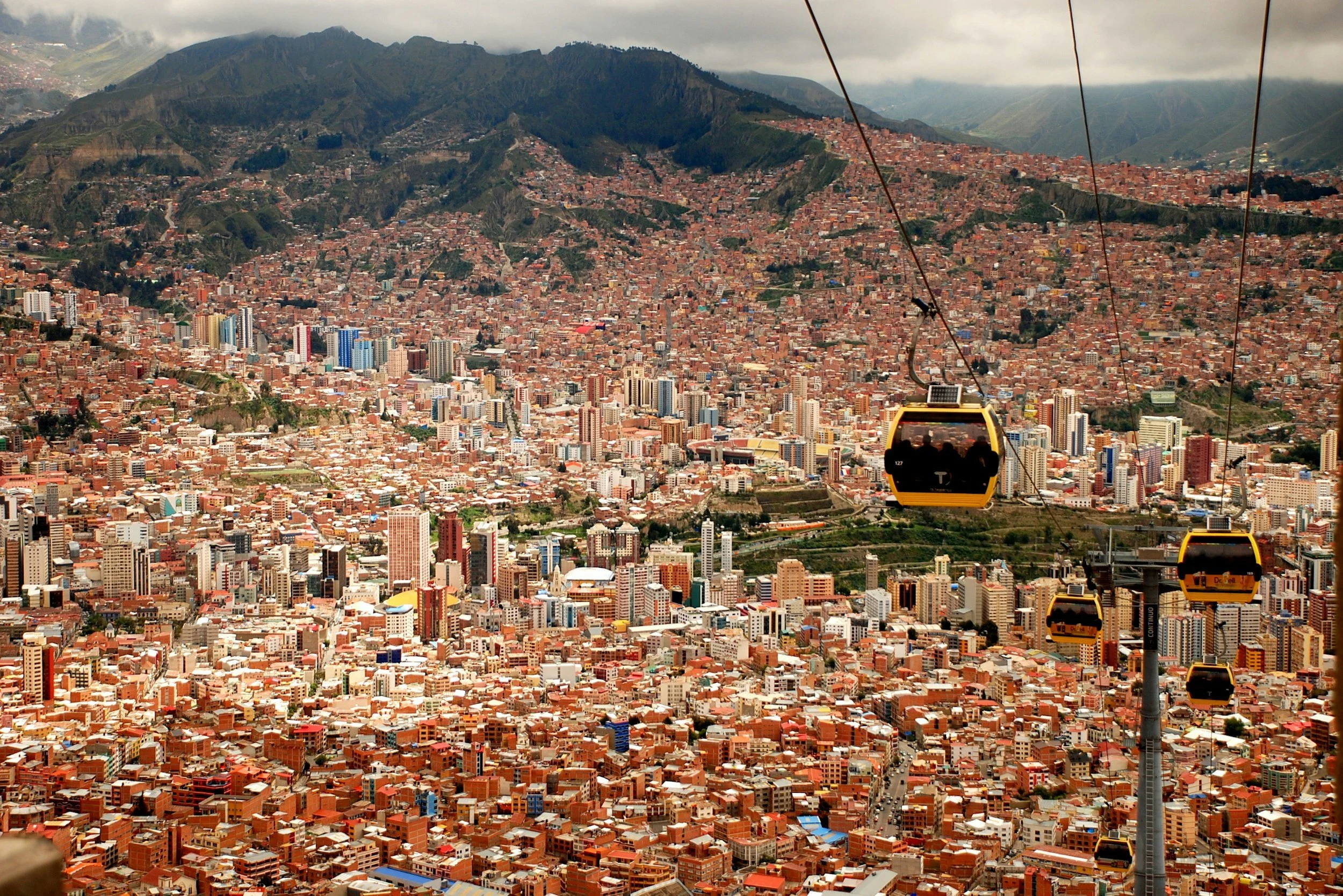 Cityscape of La Paz, Bolivia with colorful buildings, high-rise structures, and surrounding mountains viewed from a cable car ride.