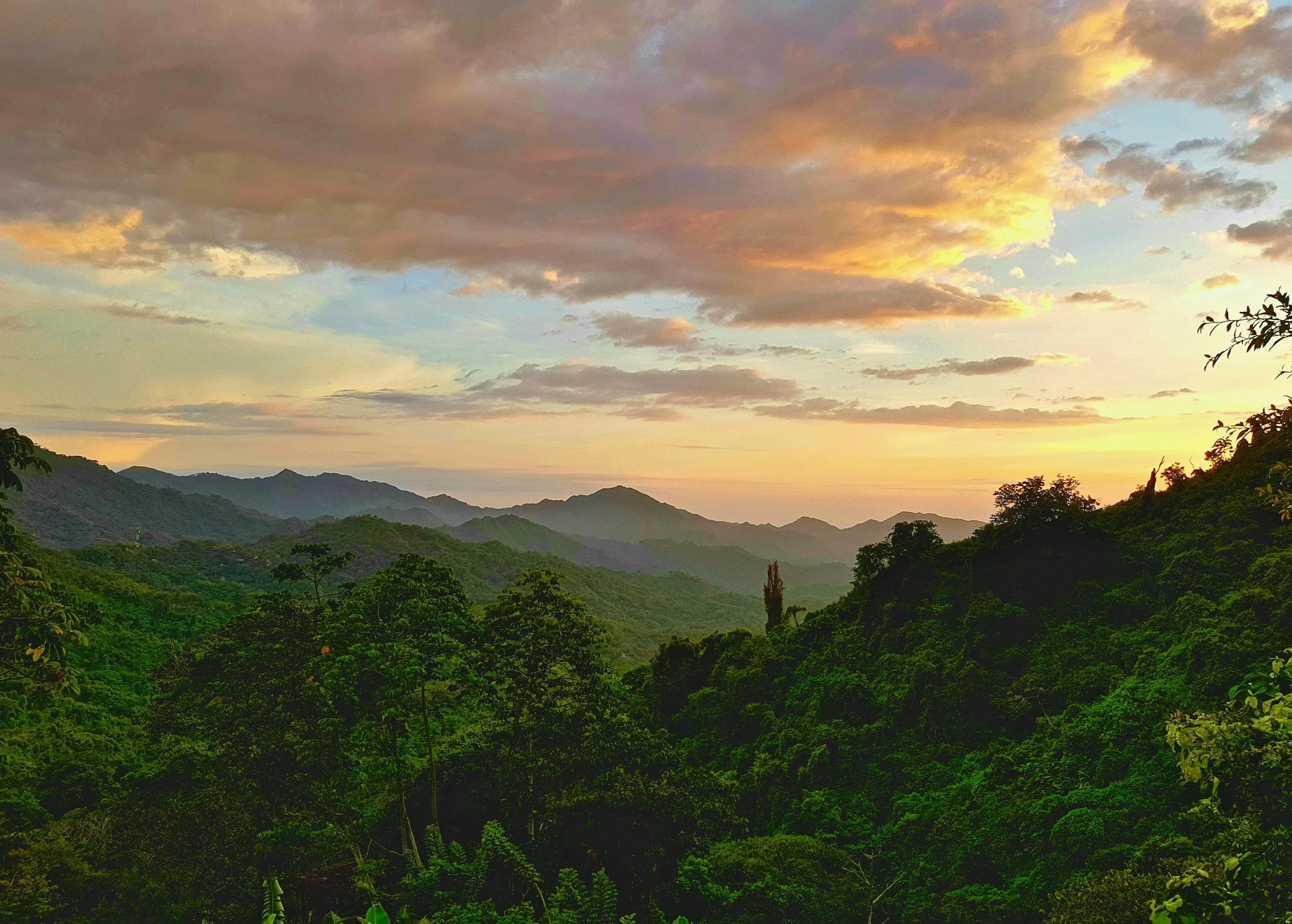 Sunset over a lush green mountain range with a cloudy sky.