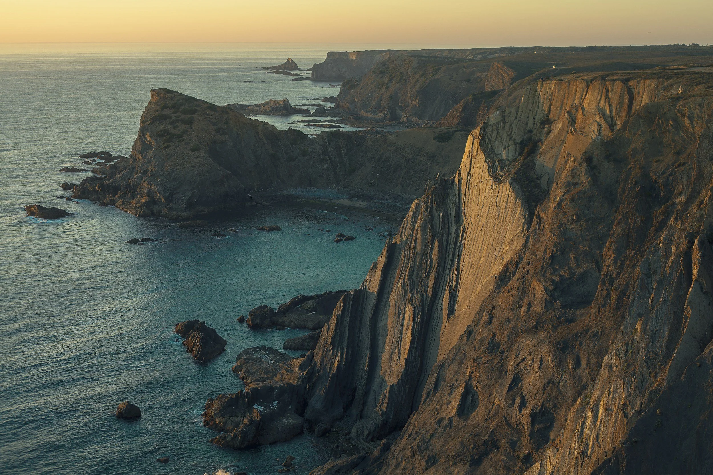 Cliffside overlooking the ocean during sunset with rocky cliffs and calm water.