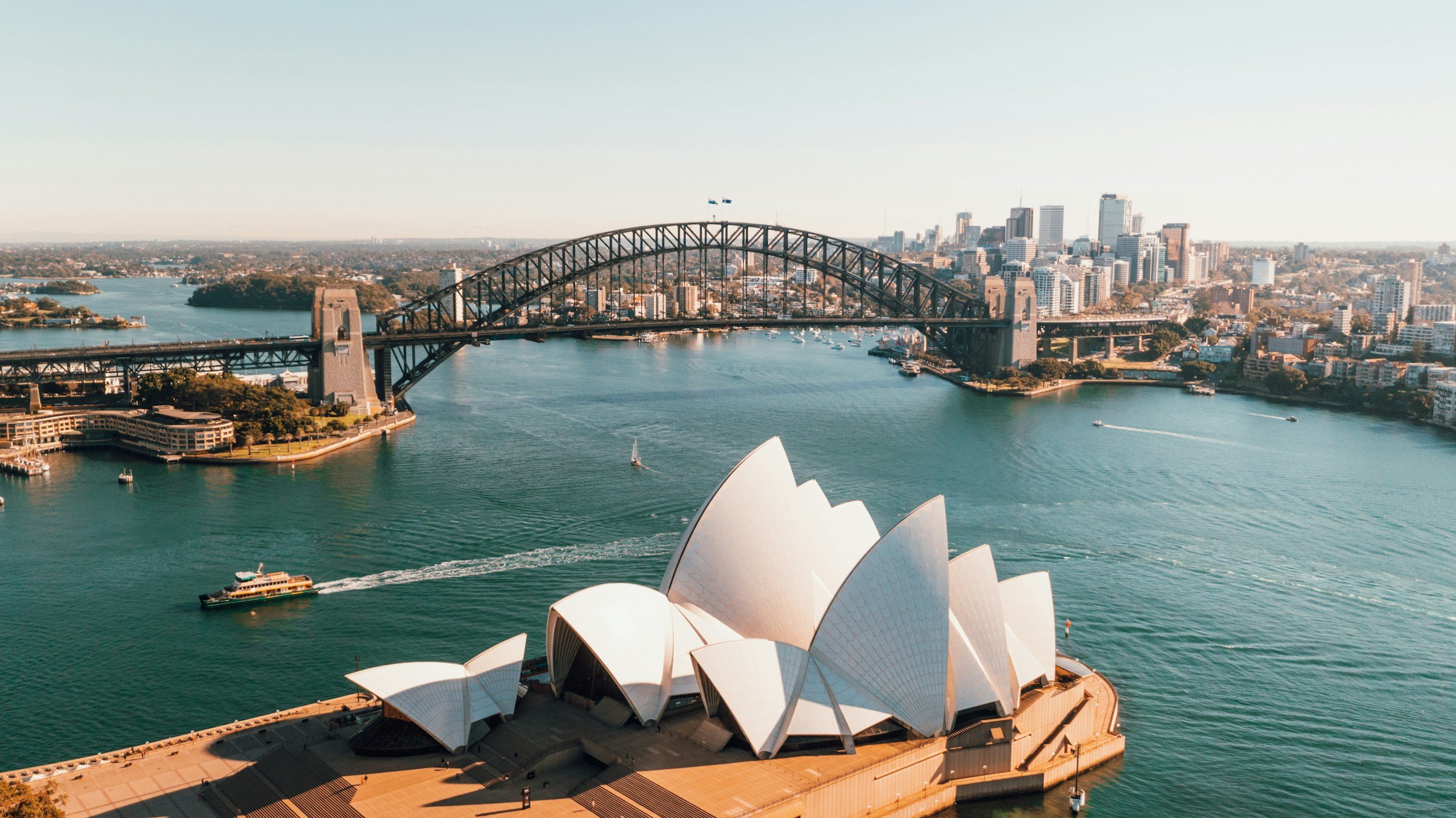 Aerial view of the Sydney Opera House and Harbour Bridge in Sydney, Australia, with water, boats, and city skyline.