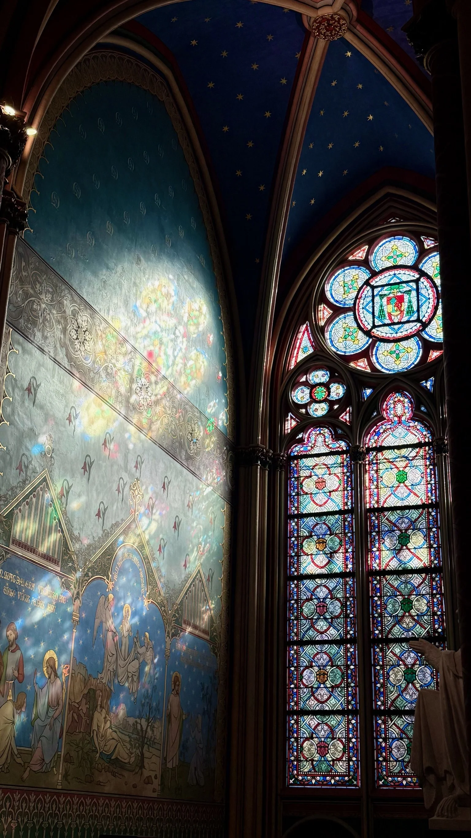 Inside a Gothic-style church with colorful stained glass windows and a painted mural depicting religious scenes.
