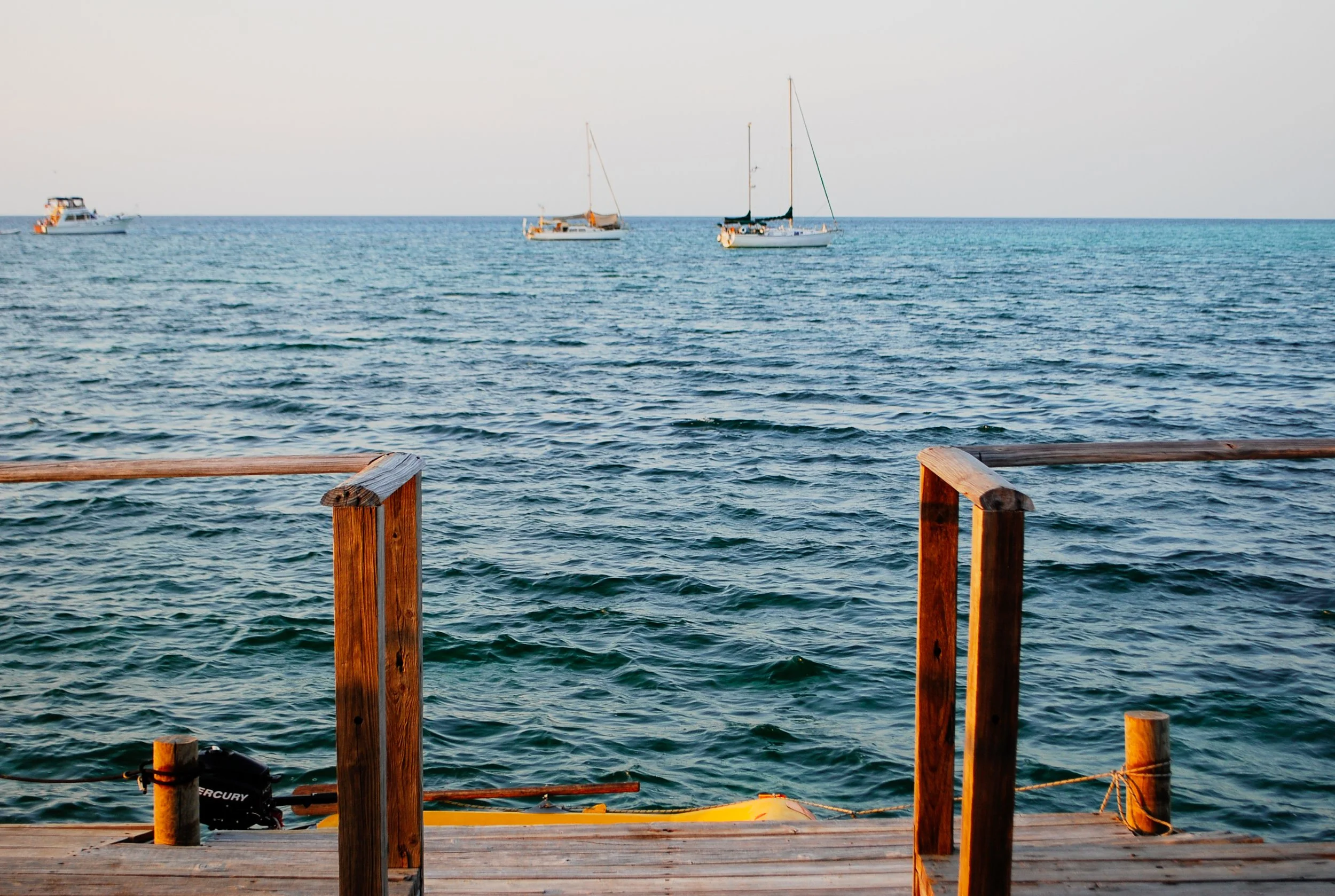 View of the ocean with three sailboats and one motorboat seen from a wooden dock with a metal railing.