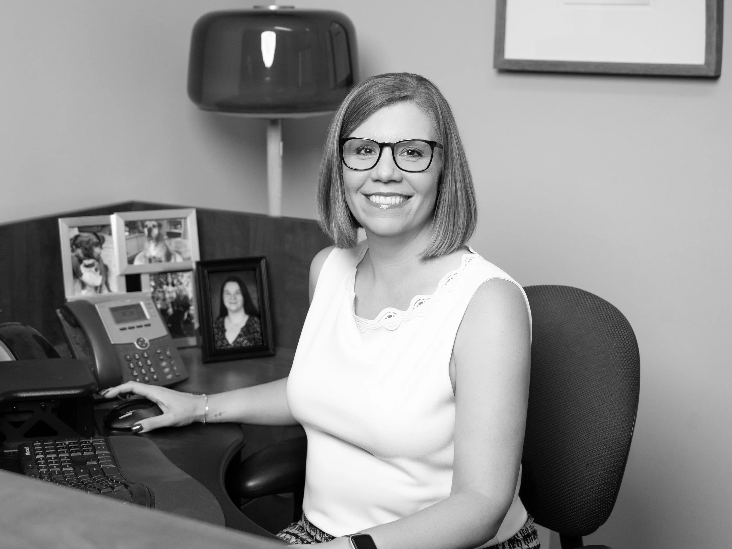 Veronica Orazio, a smiling woman with glasses sitting behind a desk with one hand on a computer mouse