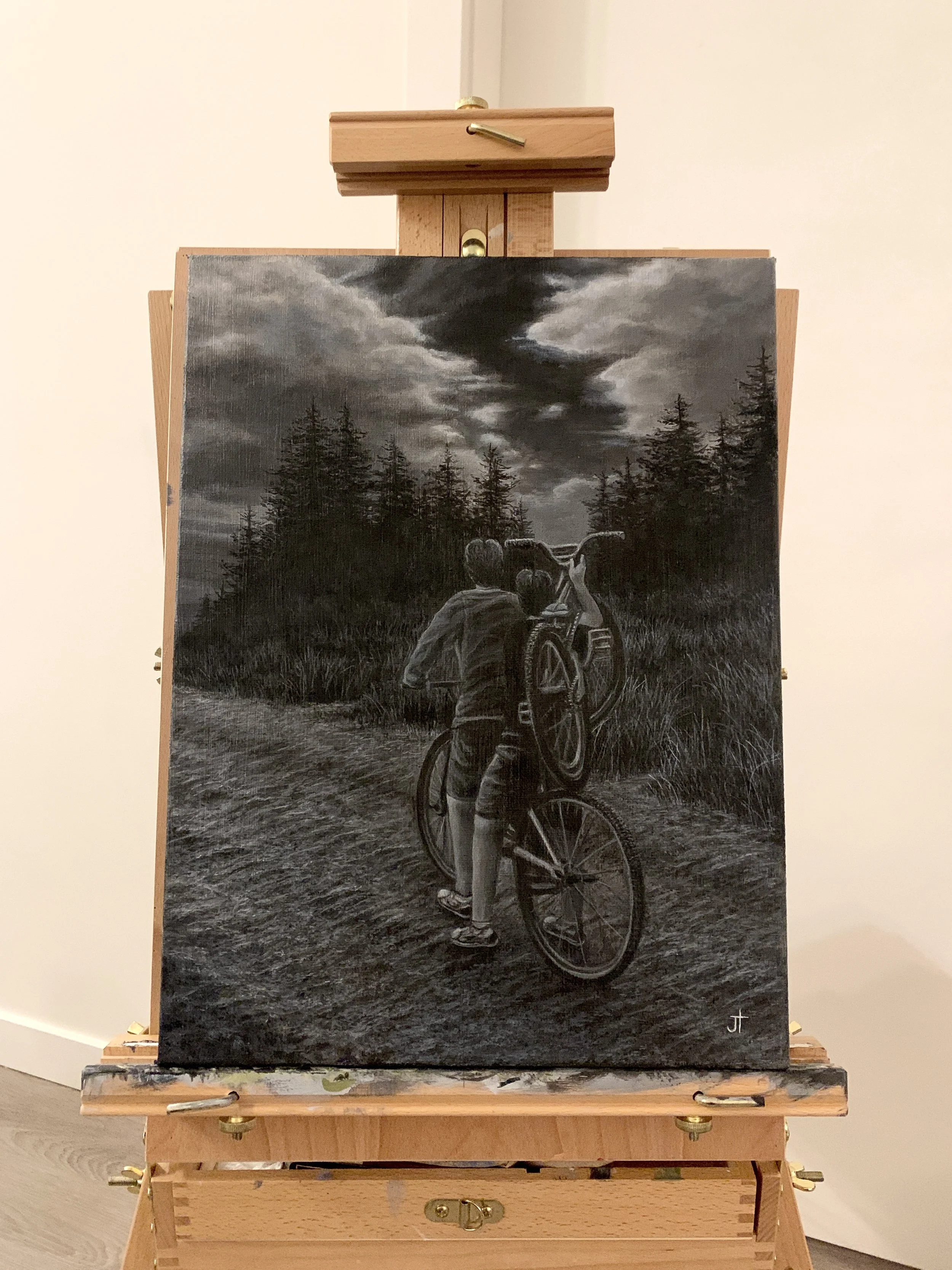 A black and white painting of a person riding a bicycle through a forested area, carrying another bicycle on their shoulder. The sky above is filled with dark, stormy clouds.