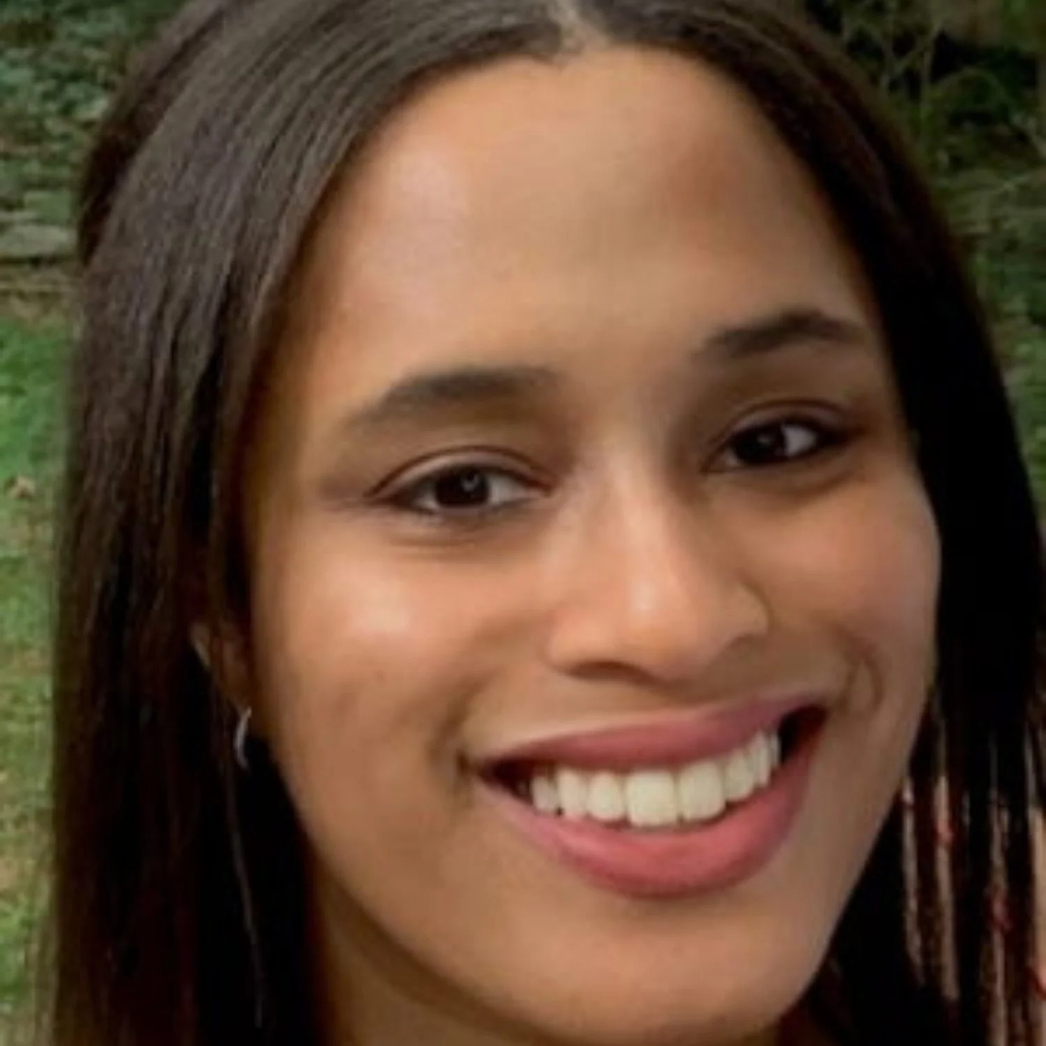 Close-up of a smiling woman with long dark hair outdoors.