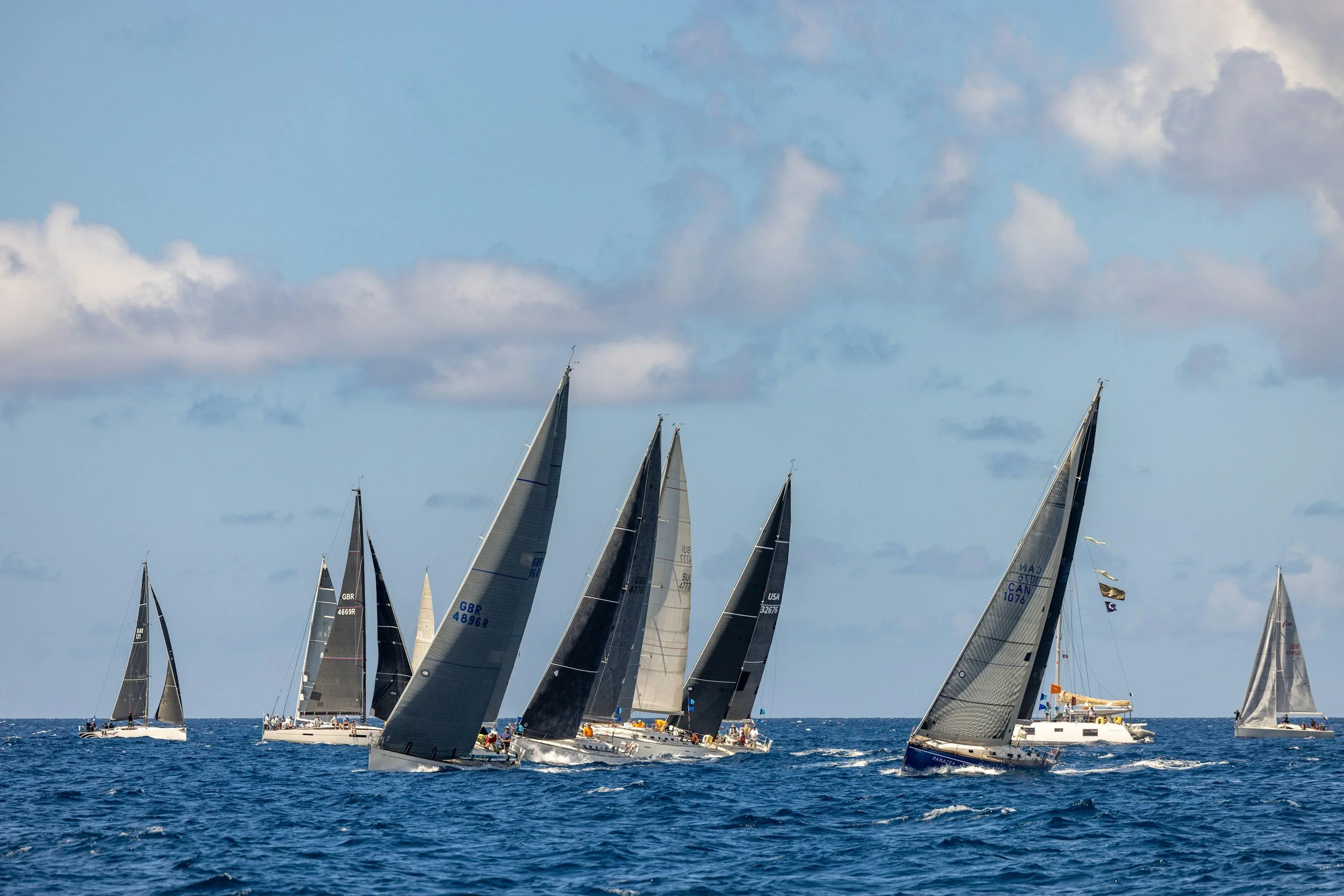 Group of six people enjoying a sailing trip on a boat in the ocean, they are smiling and raising their fists in celebration.