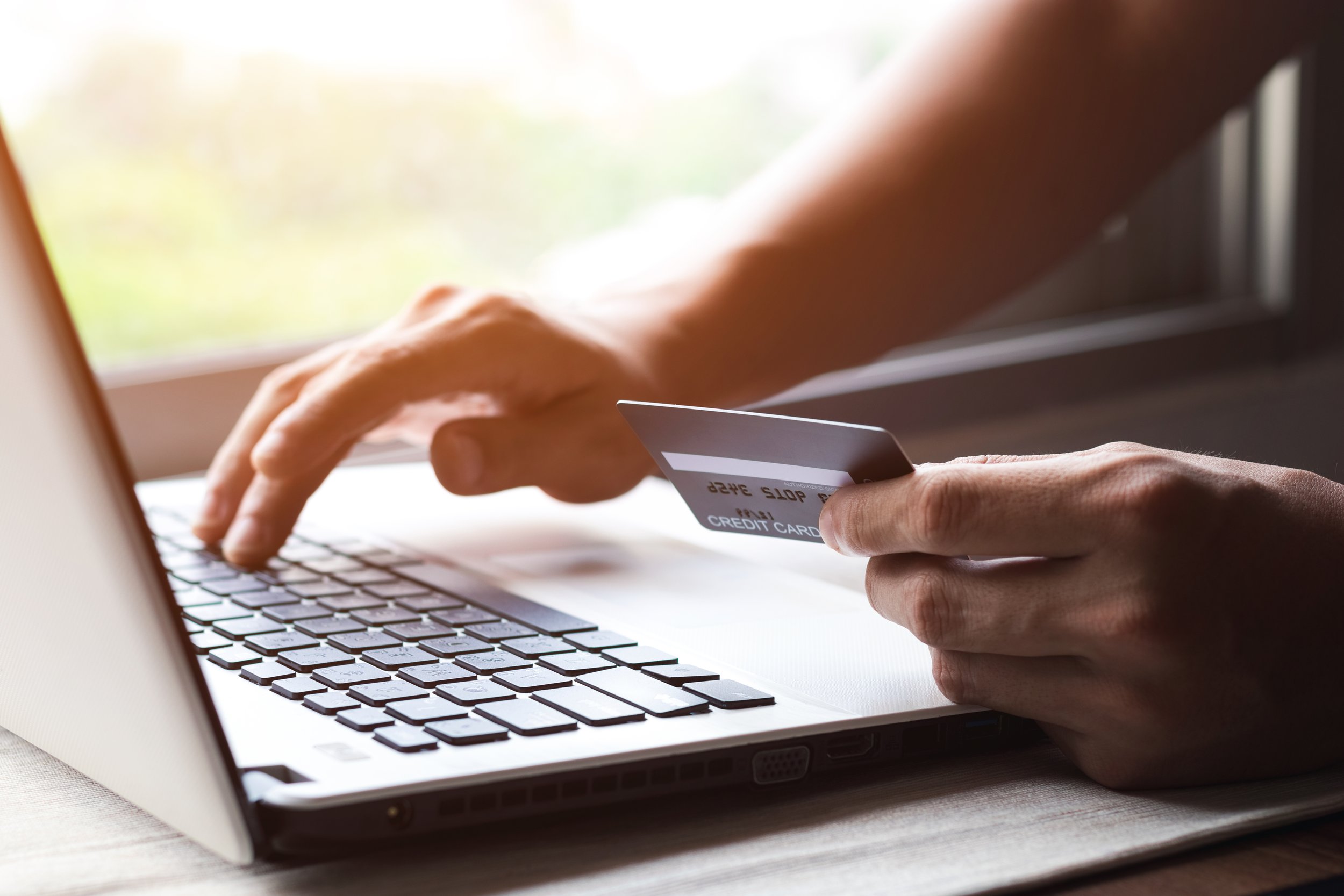 Person holding a credit card and typing on a laptop keyboard inside.