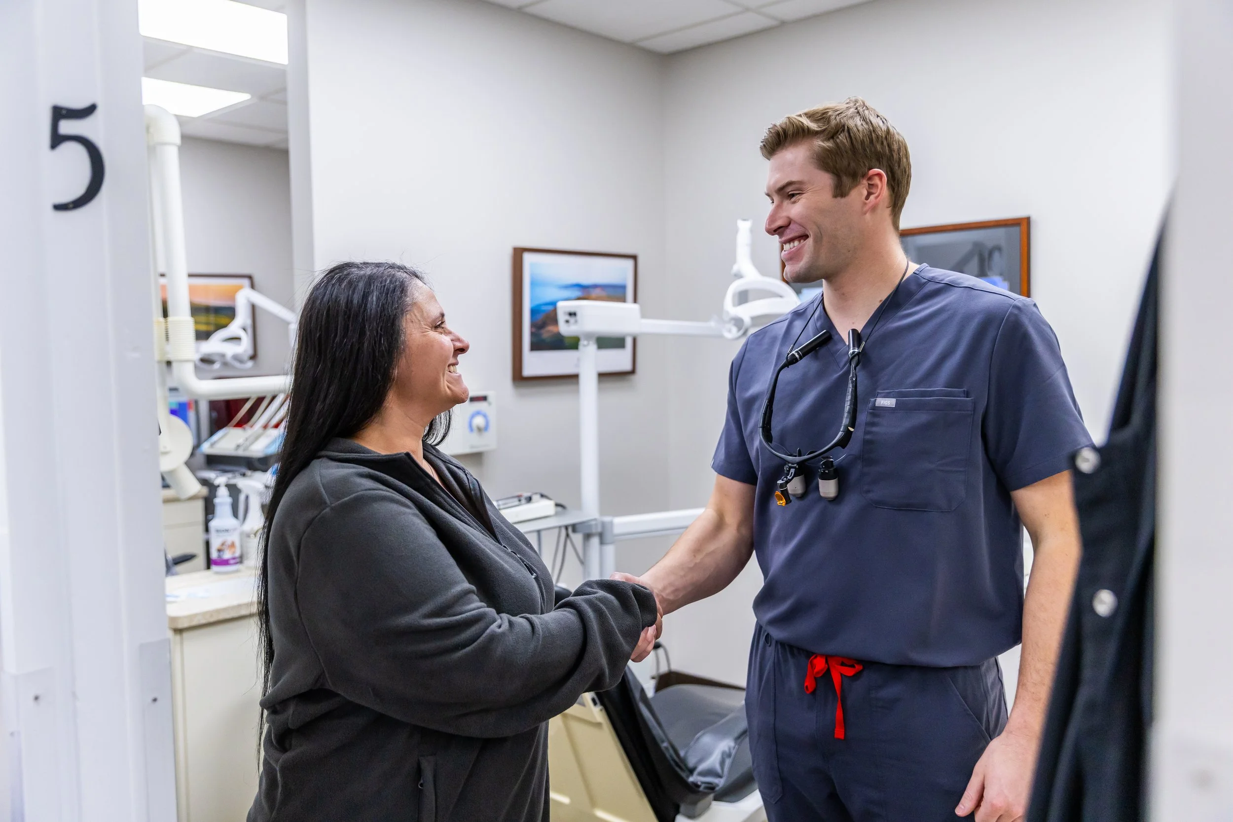 A healthcare professional and a patient shaking hands and smiling in a medical office.